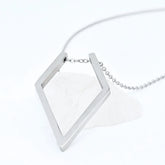 Zilveren Ring Keeper ketting van RVS met een ruitvormige hanger voor ringen, elegant gepresenteerd op een witte steen.