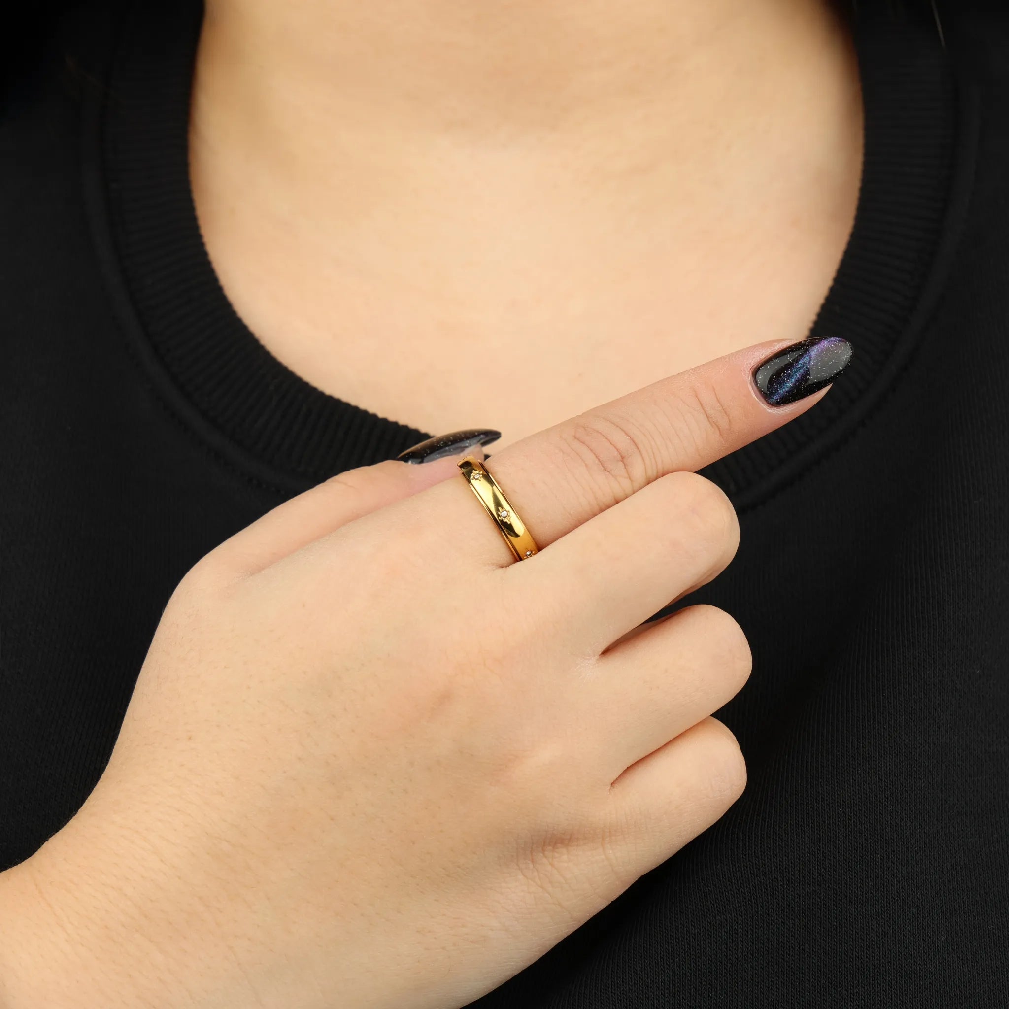 Vrouwenhand draagt gouden Adora fidget ring van RVS bij zwart shirt ter hoogte van de borst – Luminora