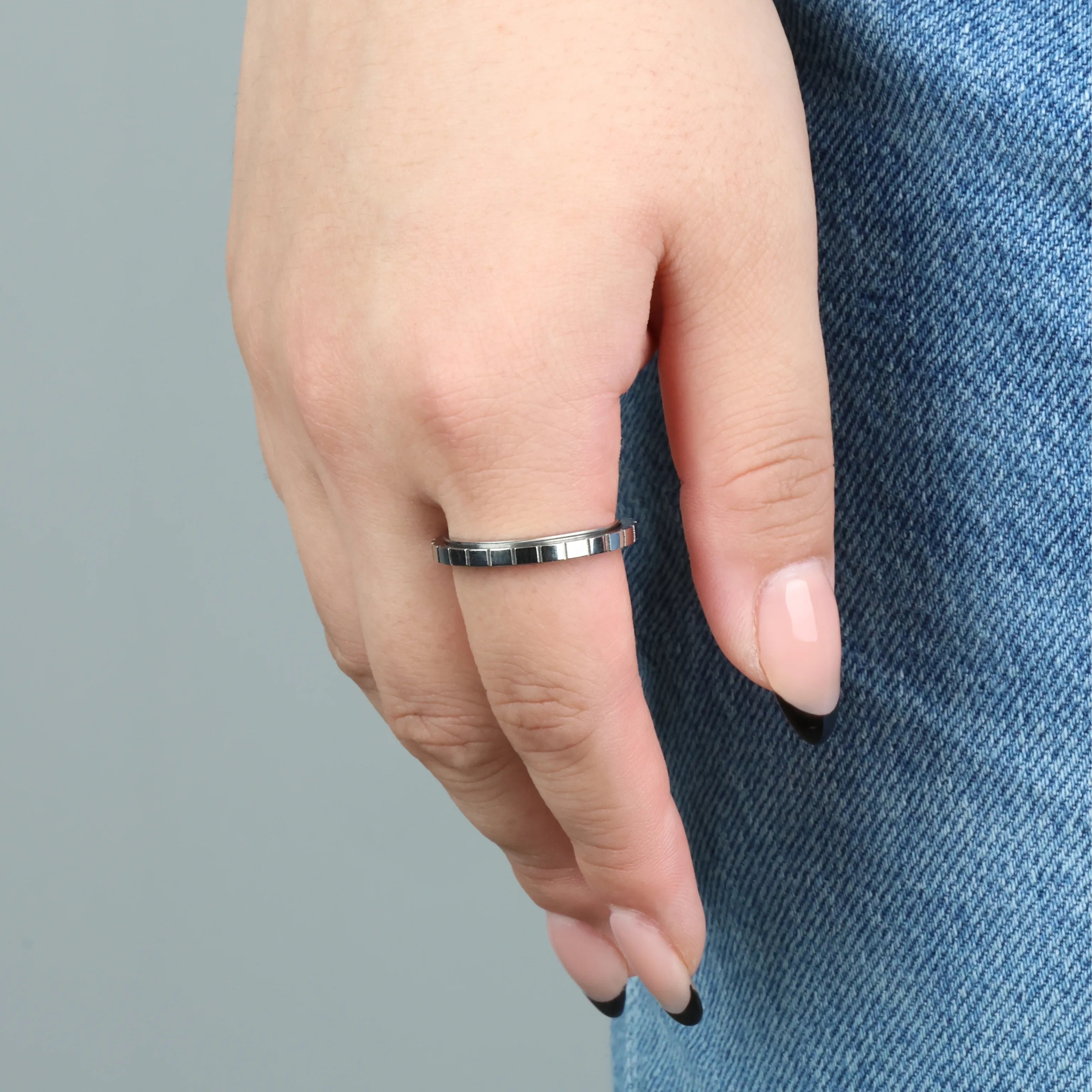 Vrouw draagt zilveren Axis fidget ring met strak groevenpatroon, hand op spijkerbroek – Luminora