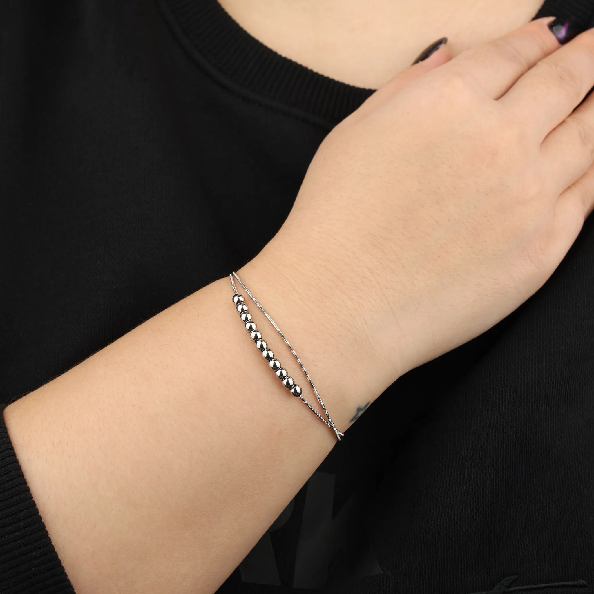 Vrouwenhand draagt zilveren Bead anxiety armband van RVS bij zwart shirt voor een rustige uitstraling – Luminora
