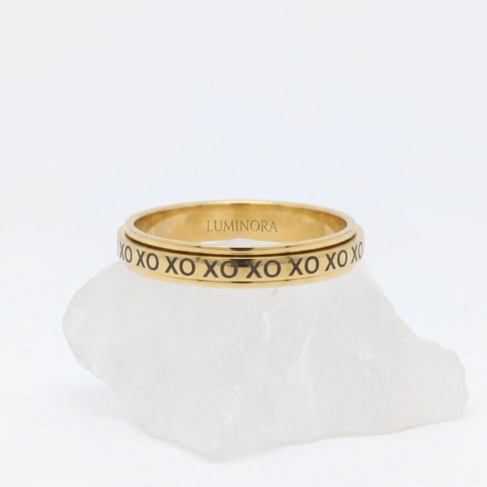 Gouden XO fidget ring van RVS met een roterend XO-design, elegant rustend op een witte steen.