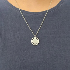 Detailopname van de zilveren Oracle anti-stress ketting van RVS, gedragen door een model in een blauwe top.