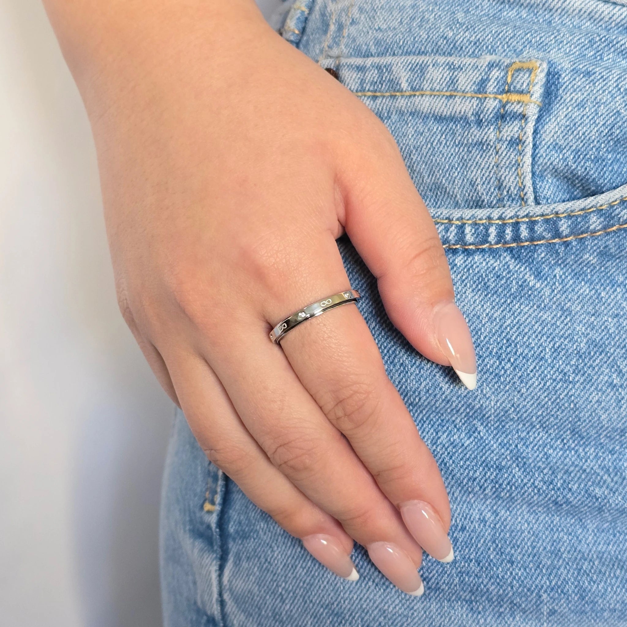 Zilveren anxiety ring met oneindigheidssymbolen gedragen om de ringvinger door een vrouw in een blauwe spijkerbroek.