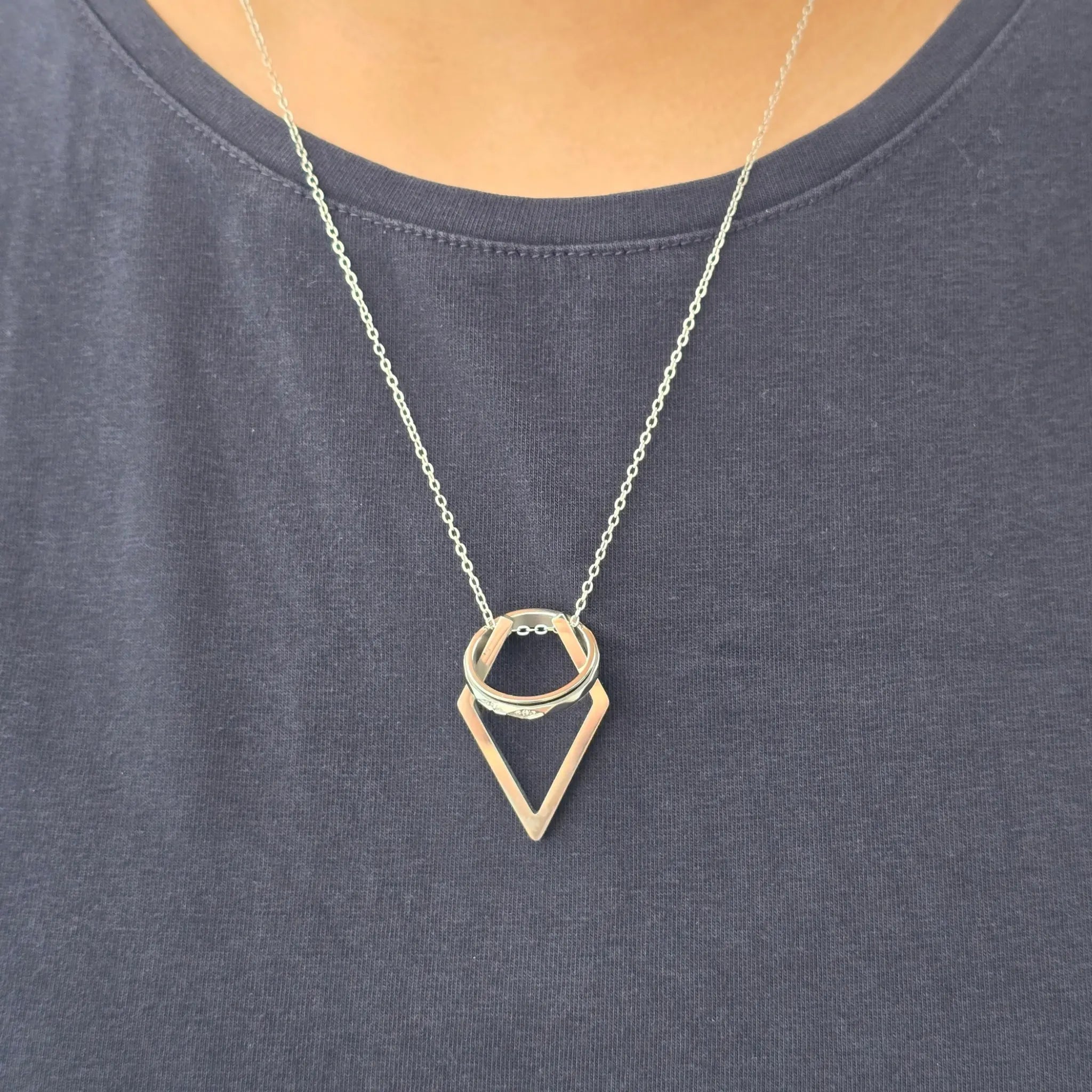 Detailopname van de zilveren Ring Keeper ketting gedragen over een blauw shirt, met een ring veilig ingehangen aan de RVS hanger.