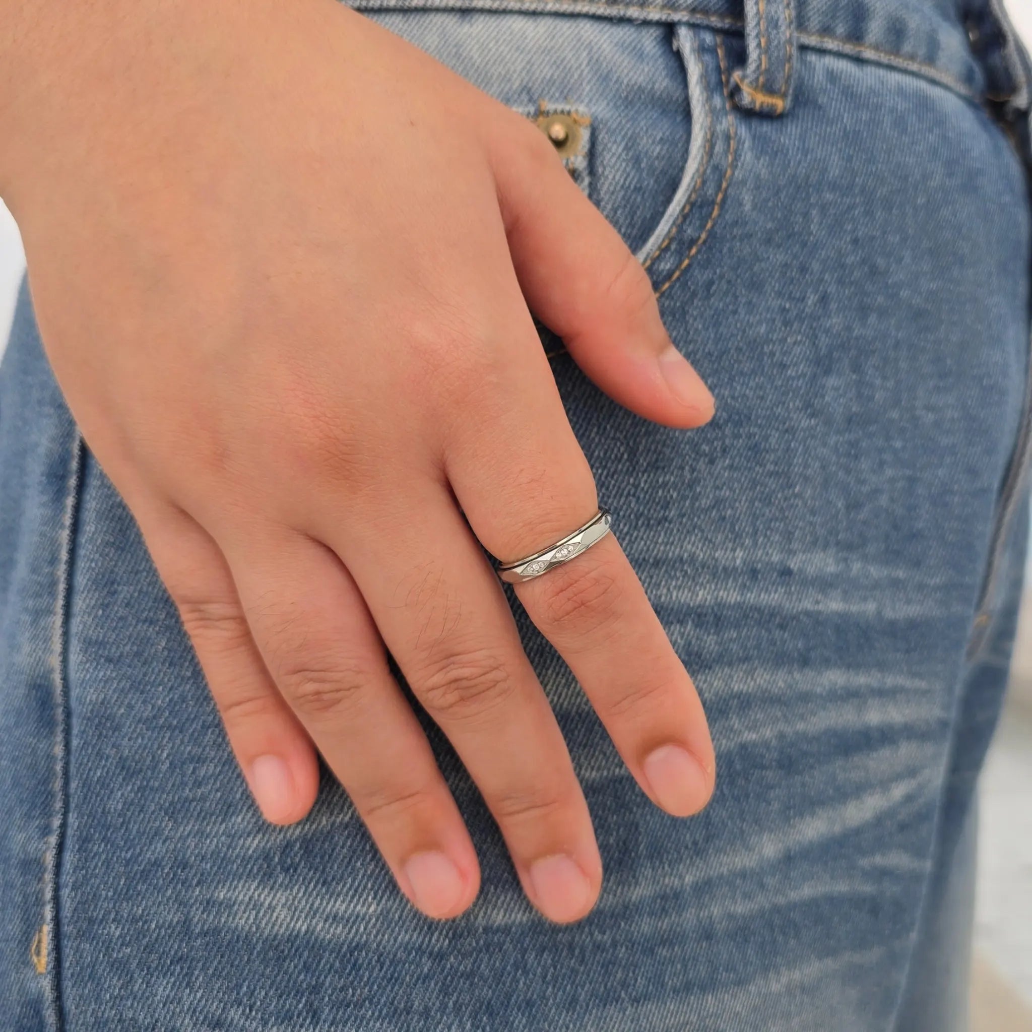Zilveren ROA anxiety ring met draaiend golfpatroon en steentjes om de vinger van een model, gefotografeerd tegen een blauwe spijkerbroek.