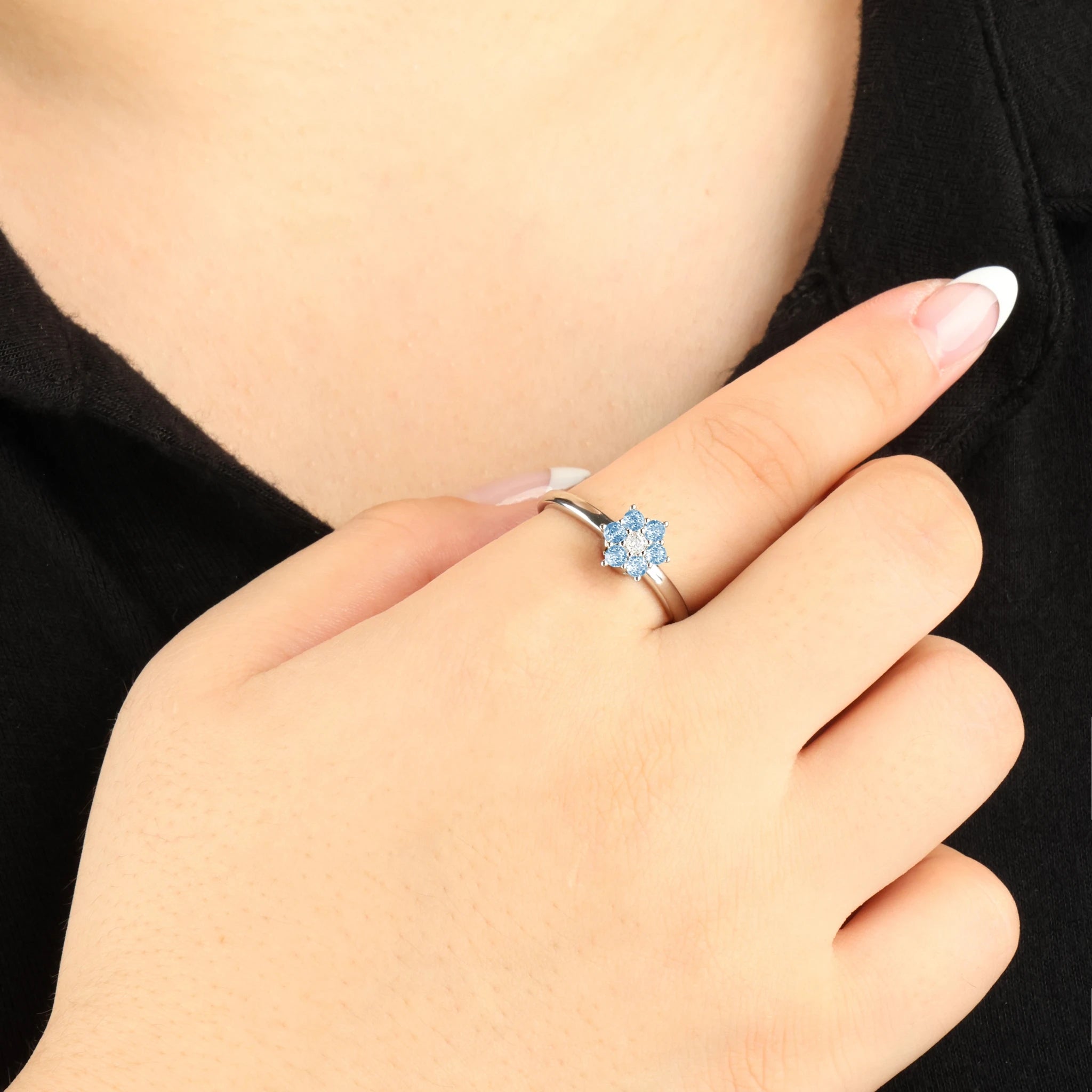 Zilveren Aqua anxiety ring met een blauw bloemetje om de vinger tegen een zwart shirt.