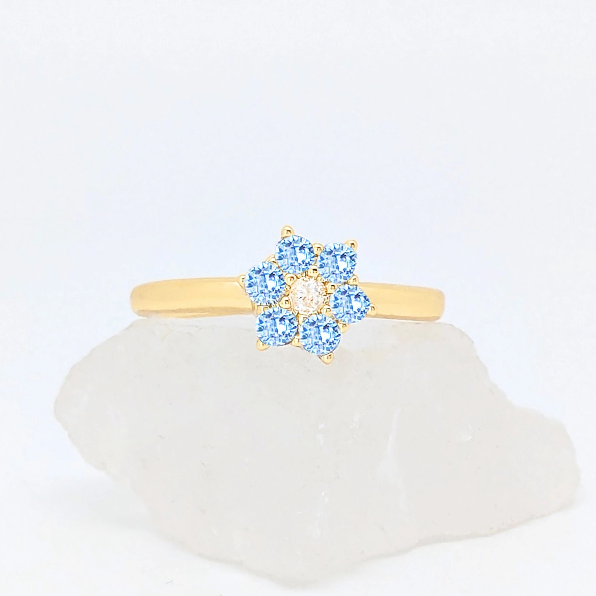 Gouden Aqua fidget ring in de vorm van een bloem met blauwe steentjes gepresenteerd op een witte steen.