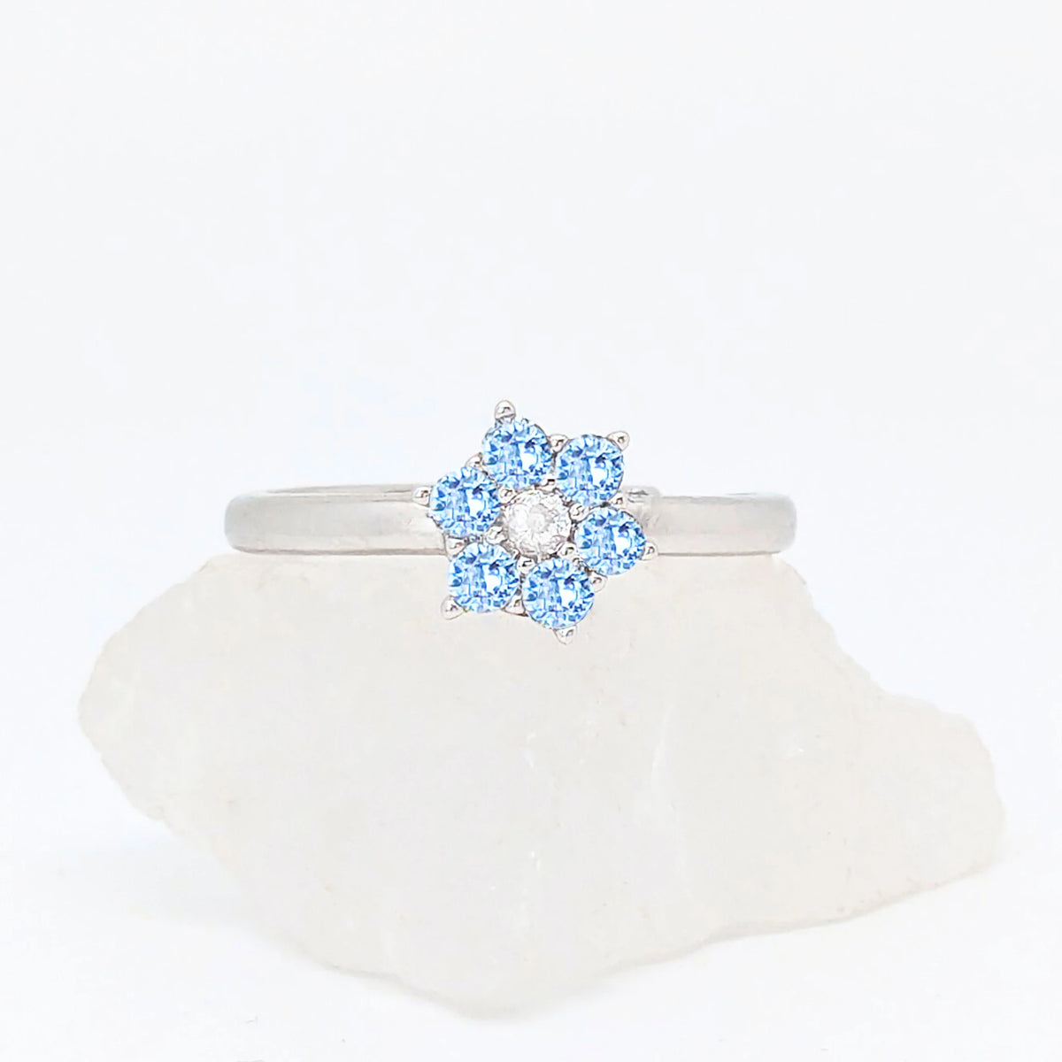 Zilveren Aqua fidget ring met een lichtblauwe bloem van kristallen liggend op een witte ruwe steen