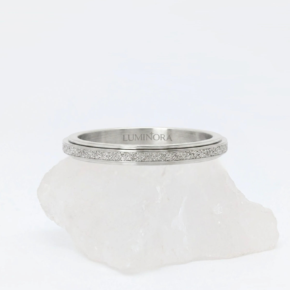 Zilveren Astra anxiety ring ontworpen als subtiele fidget ring, geplaatst op een witte kwartssteen.
