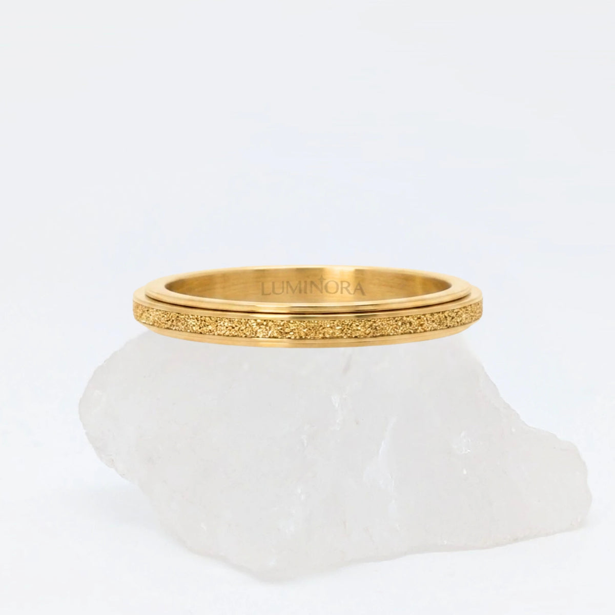 Gouden Astra fidget ring met glinsterende textuur, gepresenteerd op een witte kristallen steen.