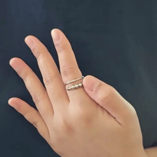 Bewegende animatie van de Punta Bead fidget ring die toont hoe de metalen kralen soepel over het gebogen spijkerdesign glijden.