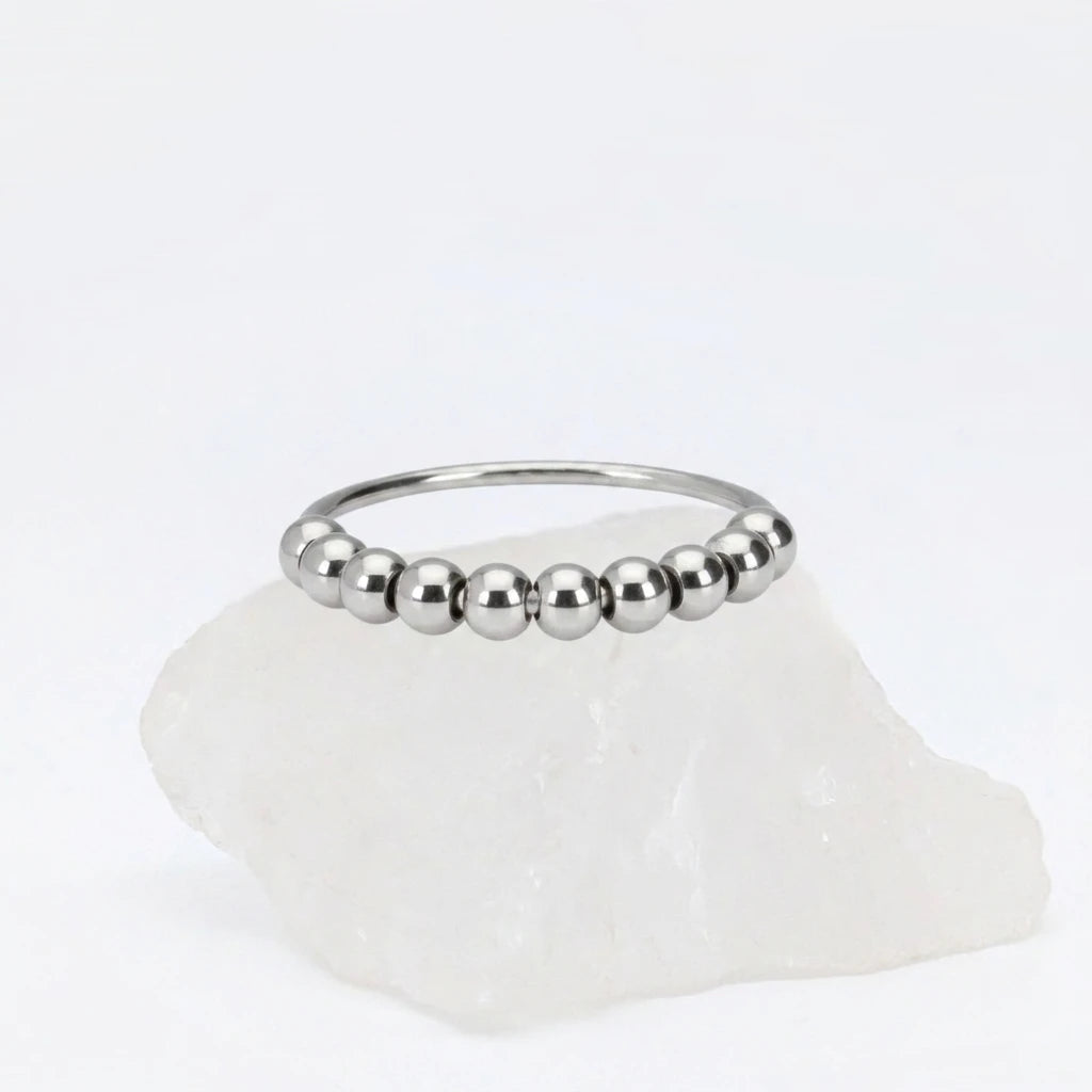 Zilveren Classic Bead fidget ring van RVS met 360 graden draaibare kralen, gepresenteerd op een witte steen.