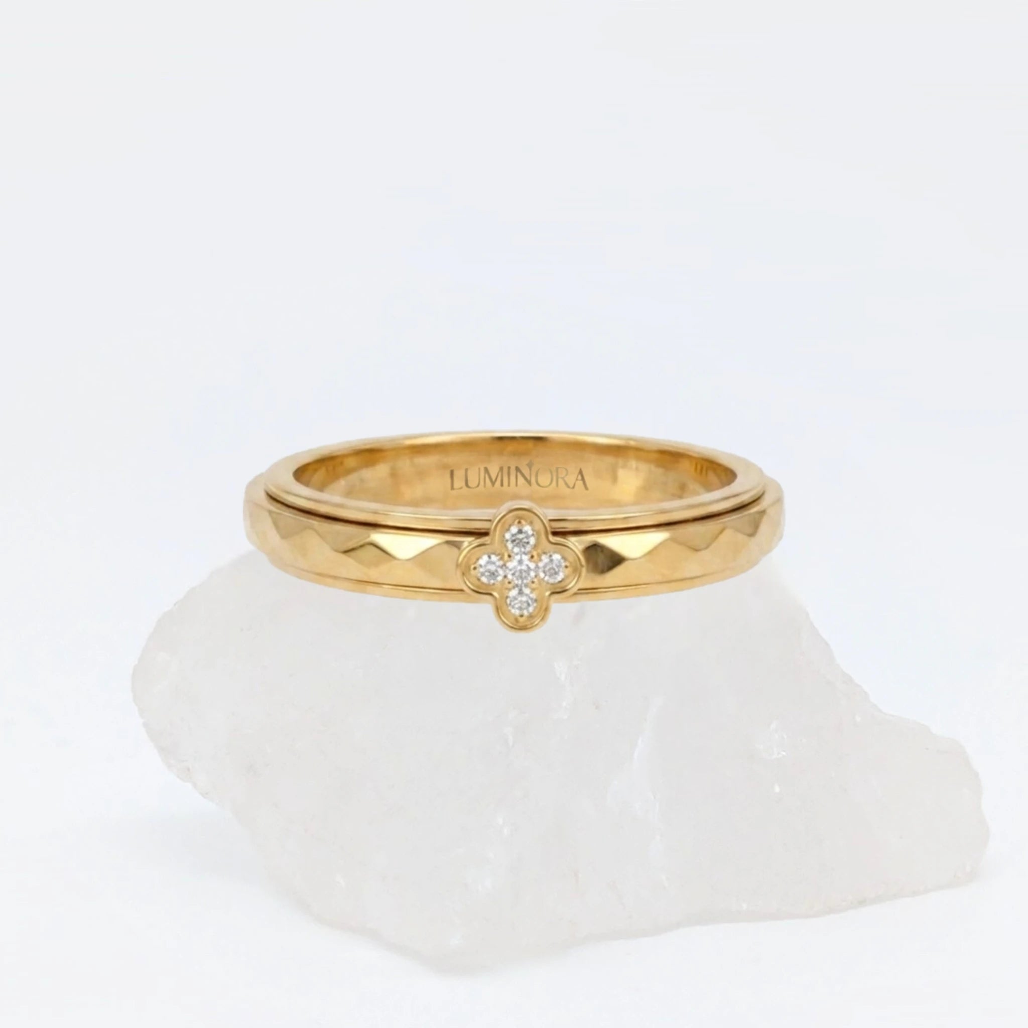 Gouden Clover fidget ring voorzien van een schitterend klavertje vier met steentjes en een ruitpatroon textuur, geplaatst op een witte steen.