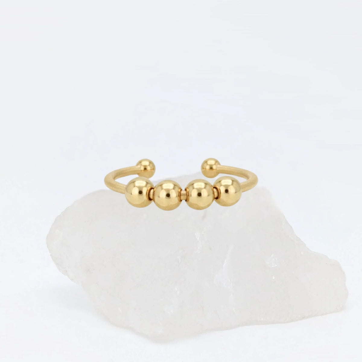 Gouden Core Bead fidget ring met vijf beweegbare balletjes, gepresenteerd op een witte kristallen steen.