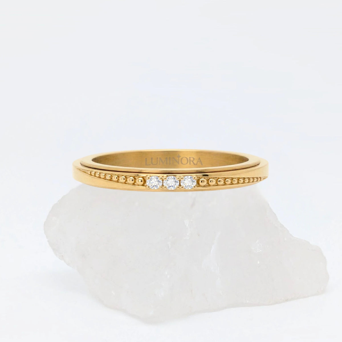 Gouden Elara fidget ring met drie subtiele kristallen en textuur, gepresenteerd op een witte steen.