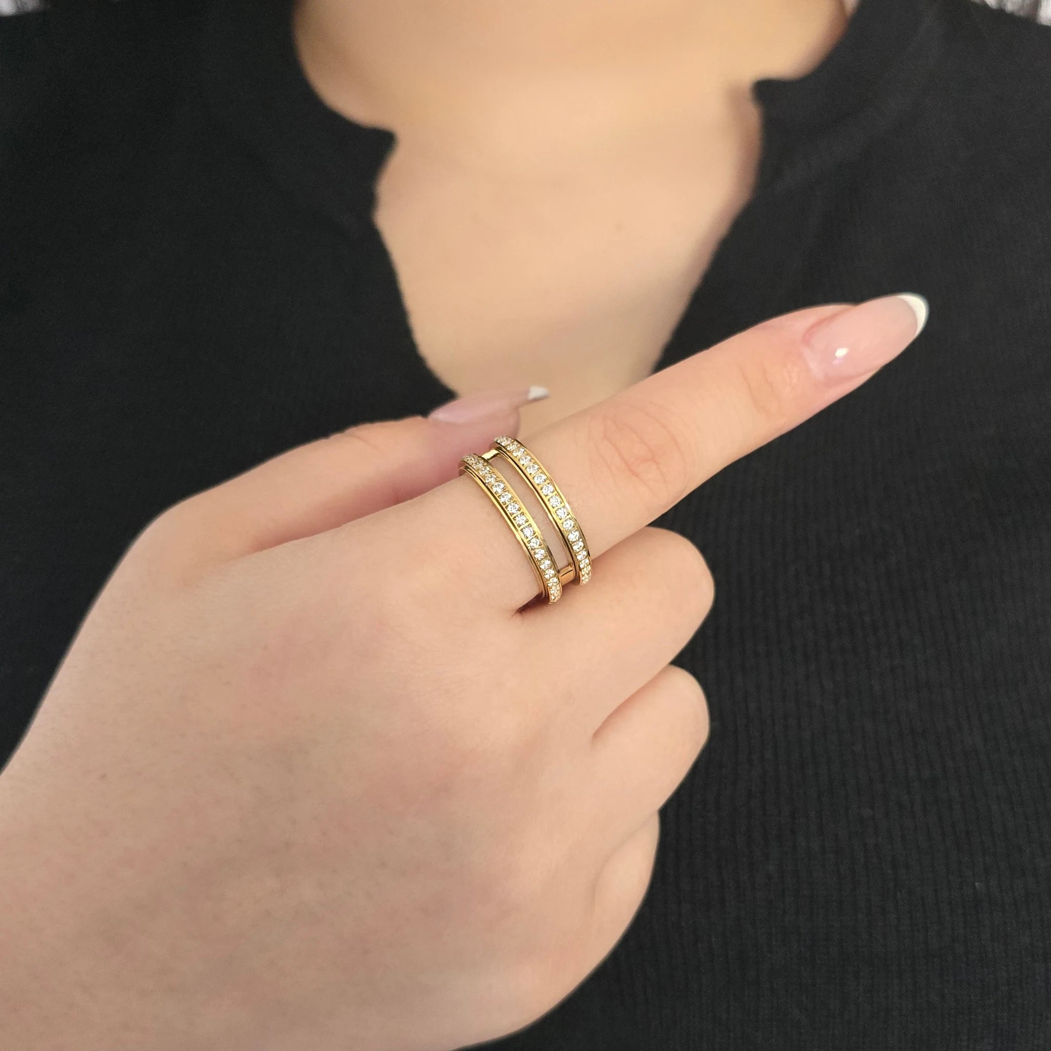 Detailopname van een gouden fidget ring met twee rijen kristallen aan de wijsvinger van een model met een zwart topje.