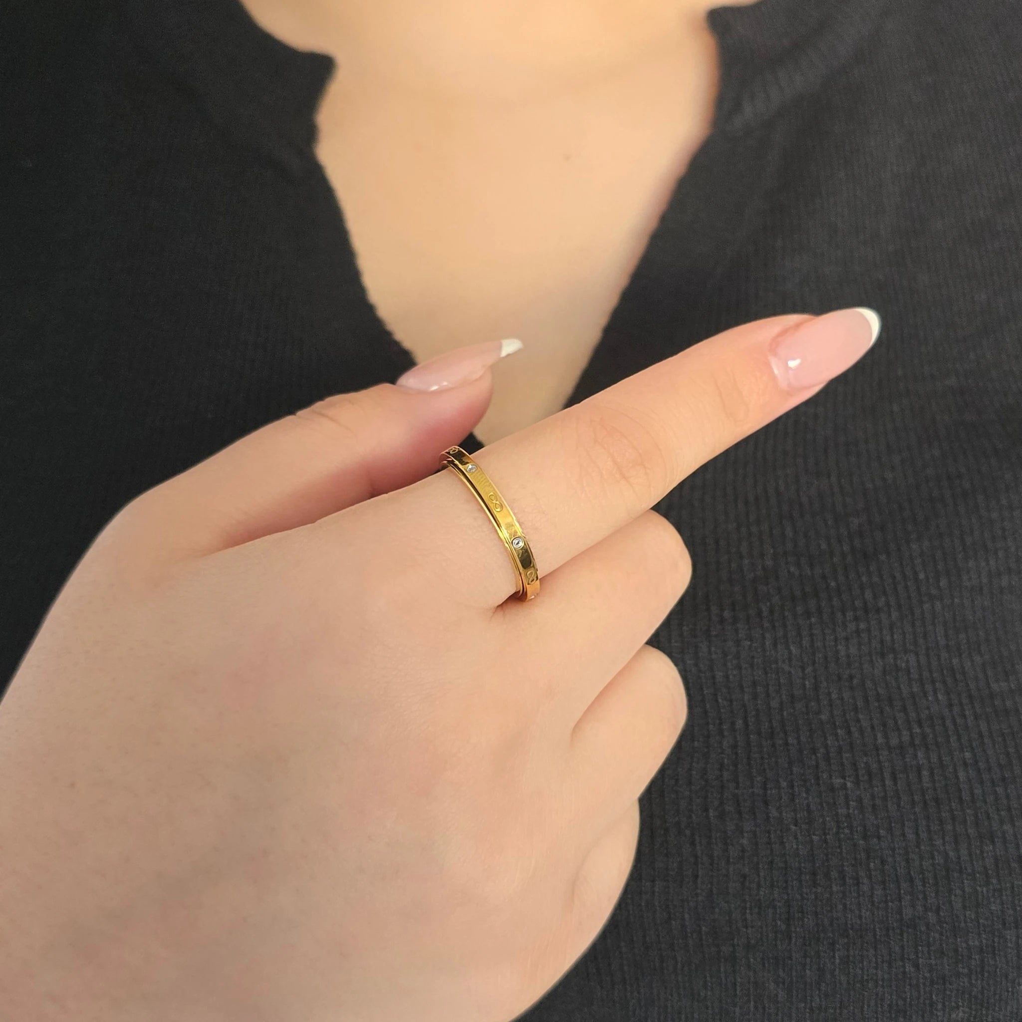 Detailopname van een gouden fidget ring met oneindigheidstekens en kristallen aan de wijsvinger van een model met een zwart topje.