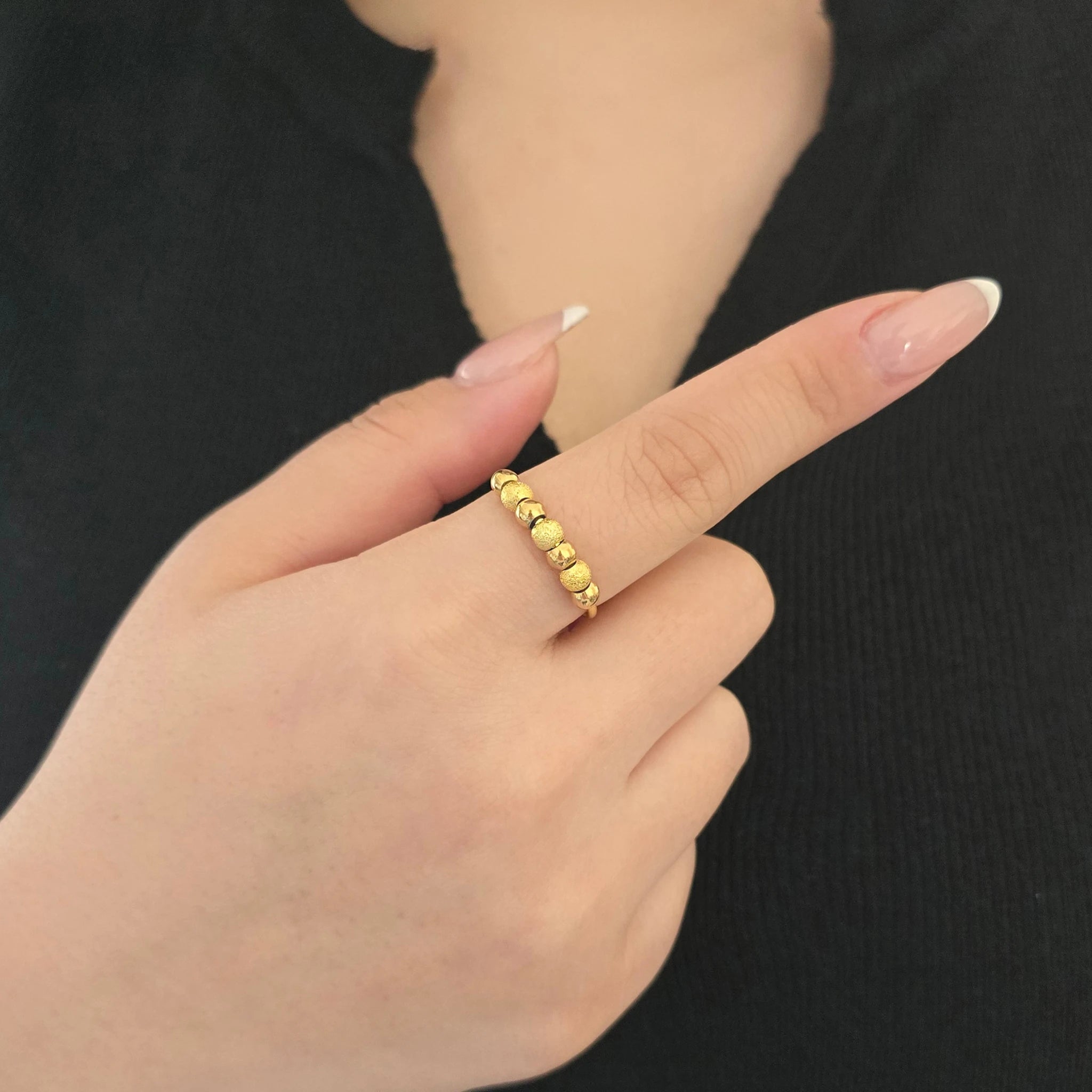 Detailopname van een gouden fidget ring met kraaltjes aan de wijsvinger van een model met een zwart topje.