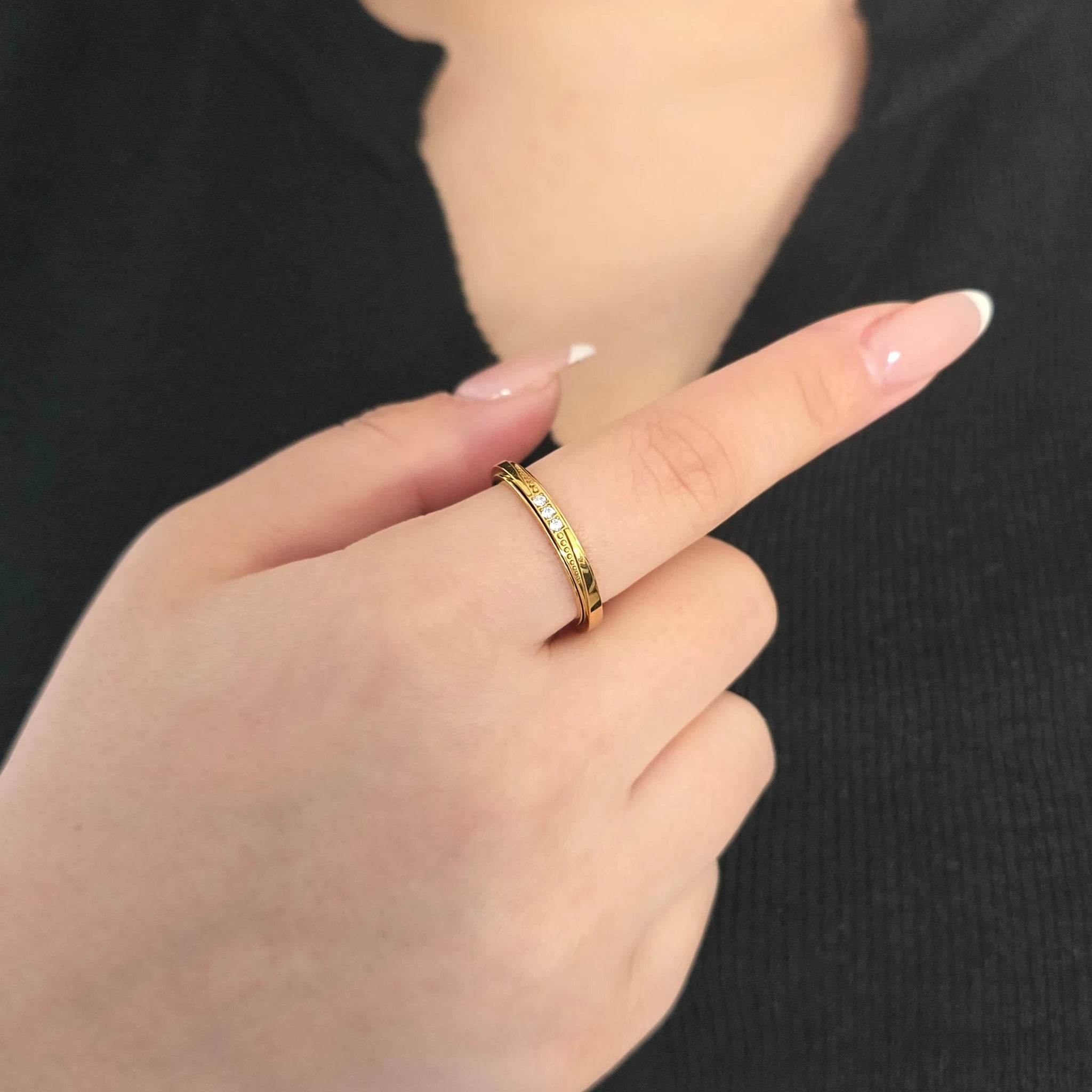 Detailopname van een gouden fidget ring met drie steentjes aan de wijsvinger van een model met een zwart topje.