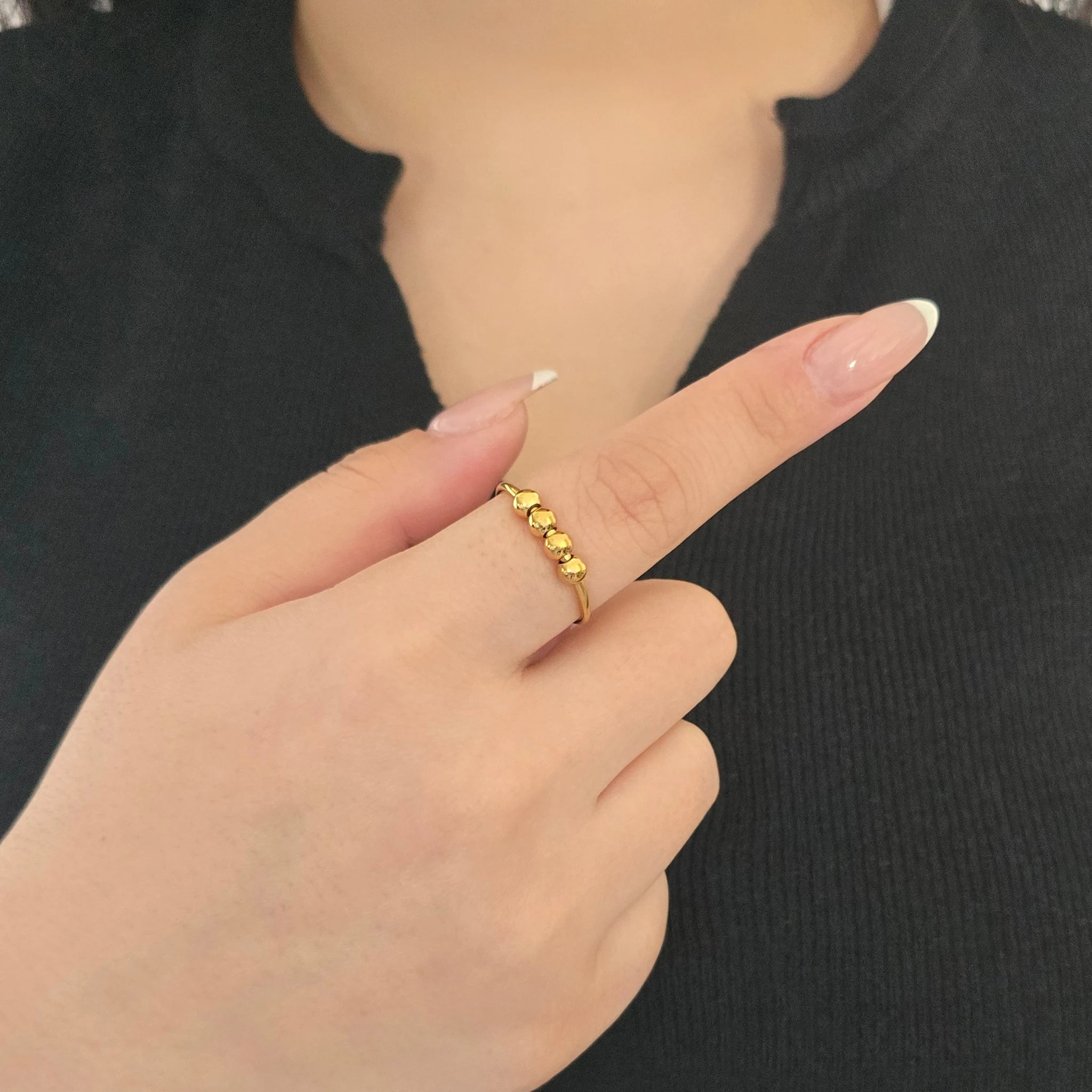Detailopname van een gouden fidget ring met balletjes aan de wijsvinger van een model met een zwart topje.