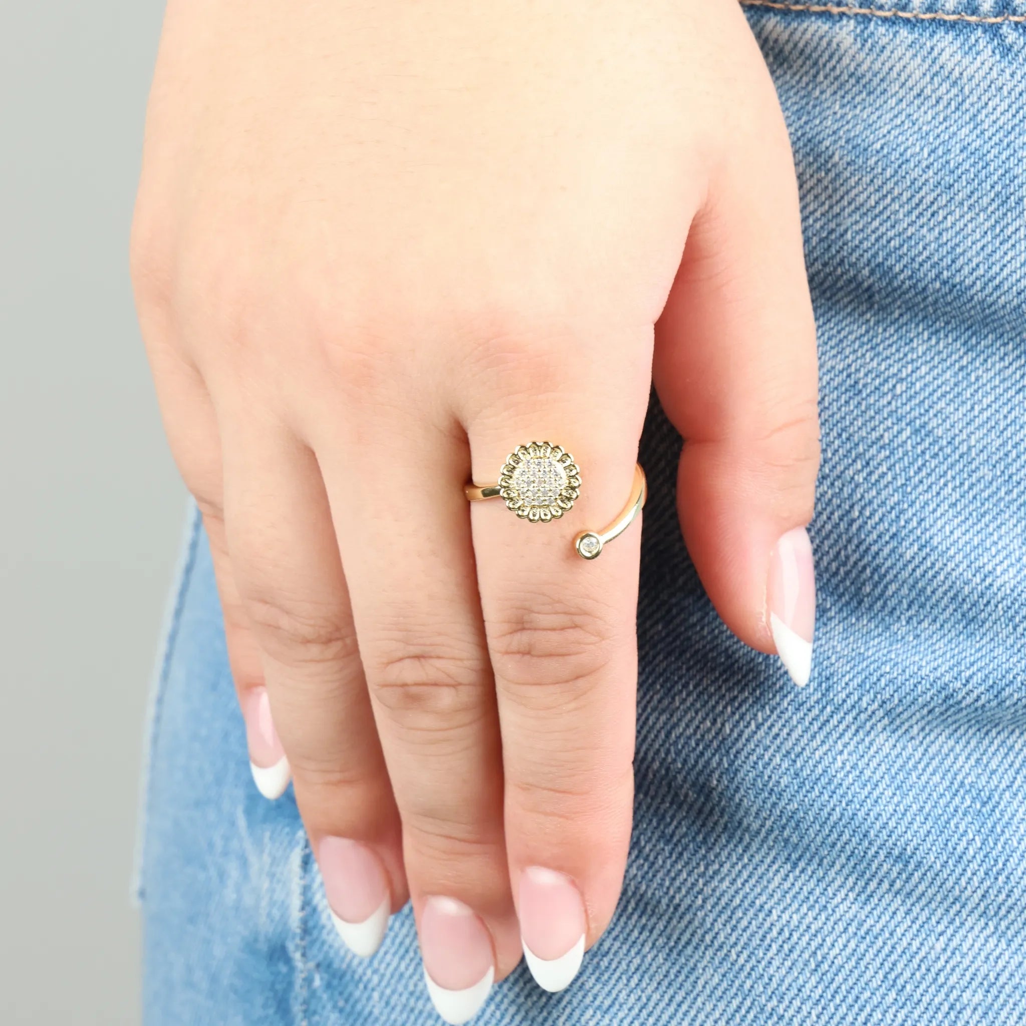 Gold plated Lotus fidget ring gedragen aan hand op jeans, verstelbaar bloemdesign met glanzend kristal