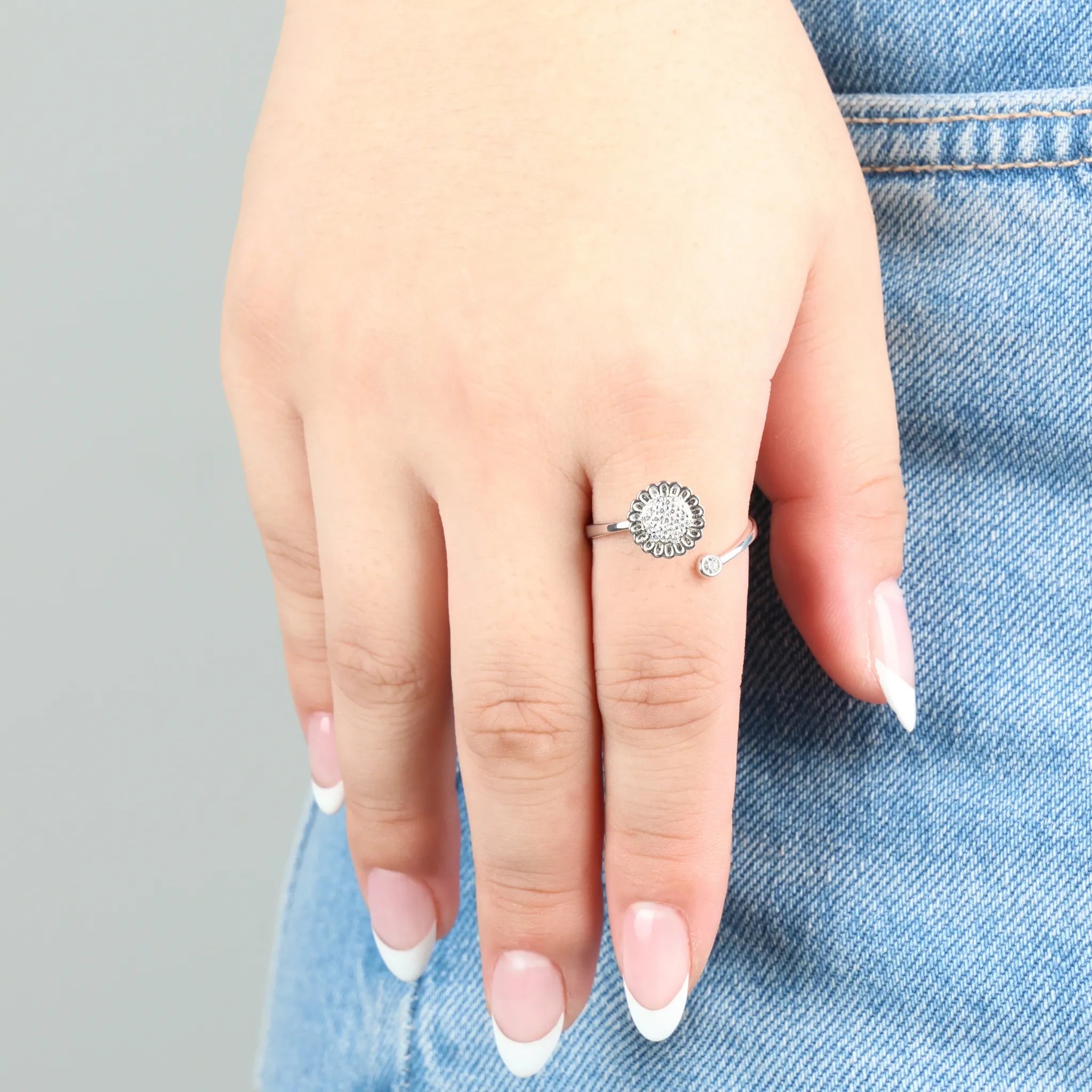 Zilverkleurige Lotus fidget ring gedragen aan hand op denim jeans, verstelbaar silver plated design met bloemdetail