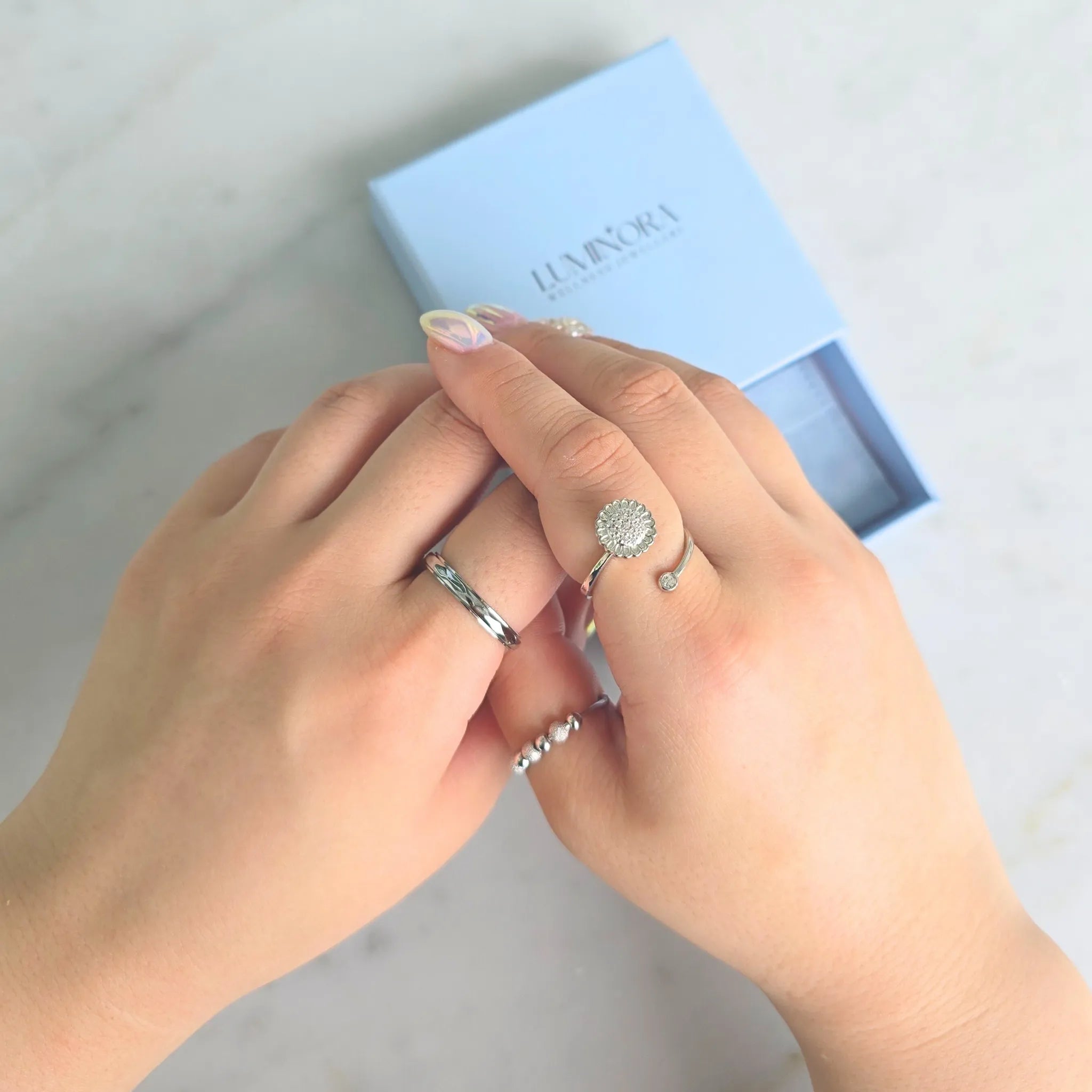 erstelbare zilverkleurige Lotus fidget ring met bloemvormig design en kristal, gedragen aan de hand met Luminora sieradendoosje op de achtergrond – silver plated wellness ring