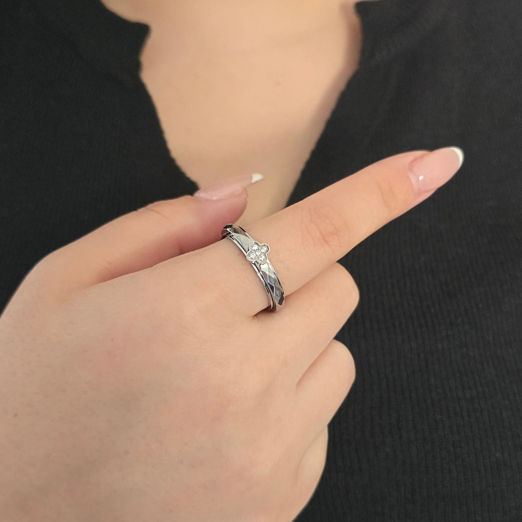 Detailopname van een zilveren Clover fidget ring met ingelegde kristallen aan de wijsvinger van een model met een zwart topje.
