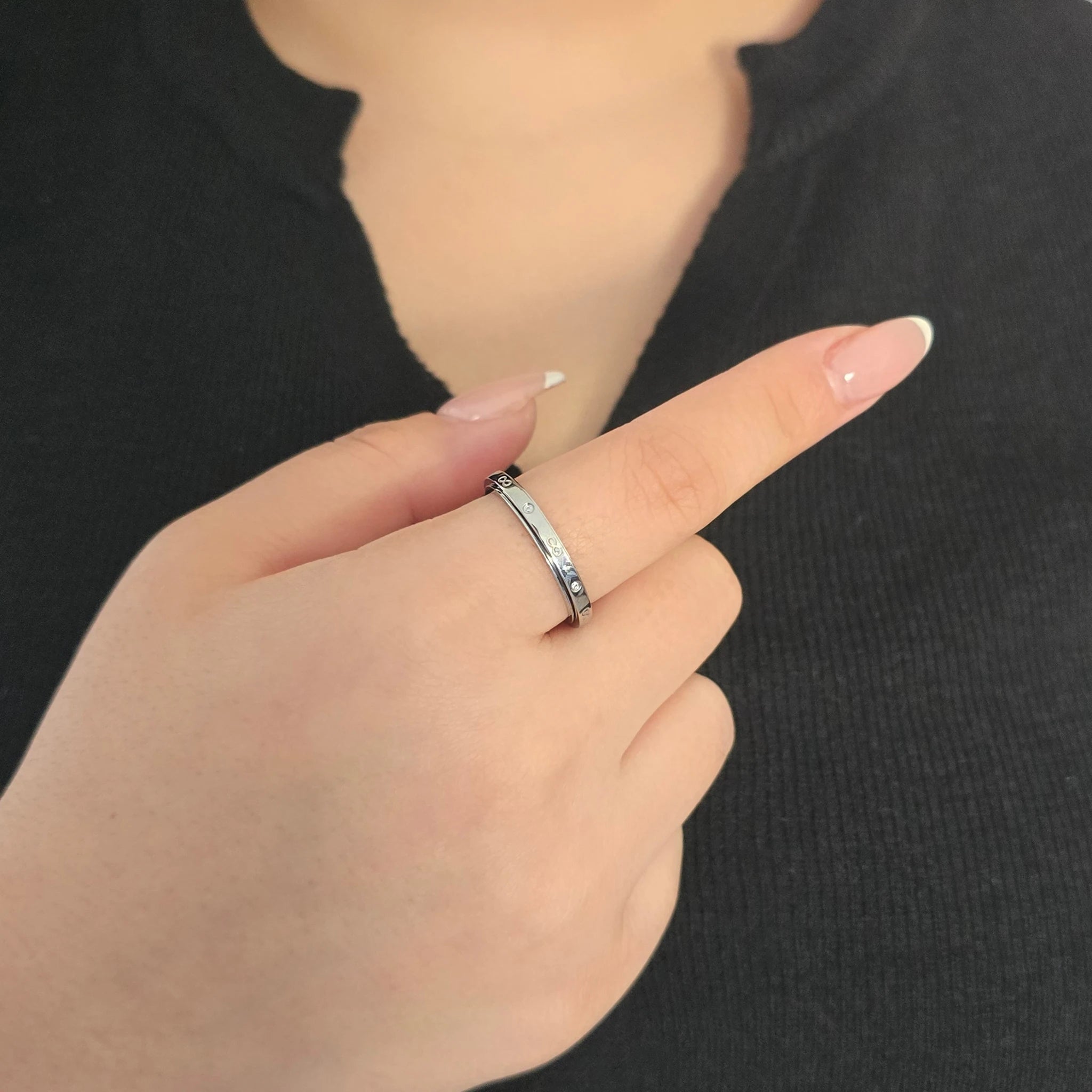 Elegante zilveren fidget ring met subtiele infinity symbolen en fonkelende steentjes, gedragen door een model met een chique zwart topje.