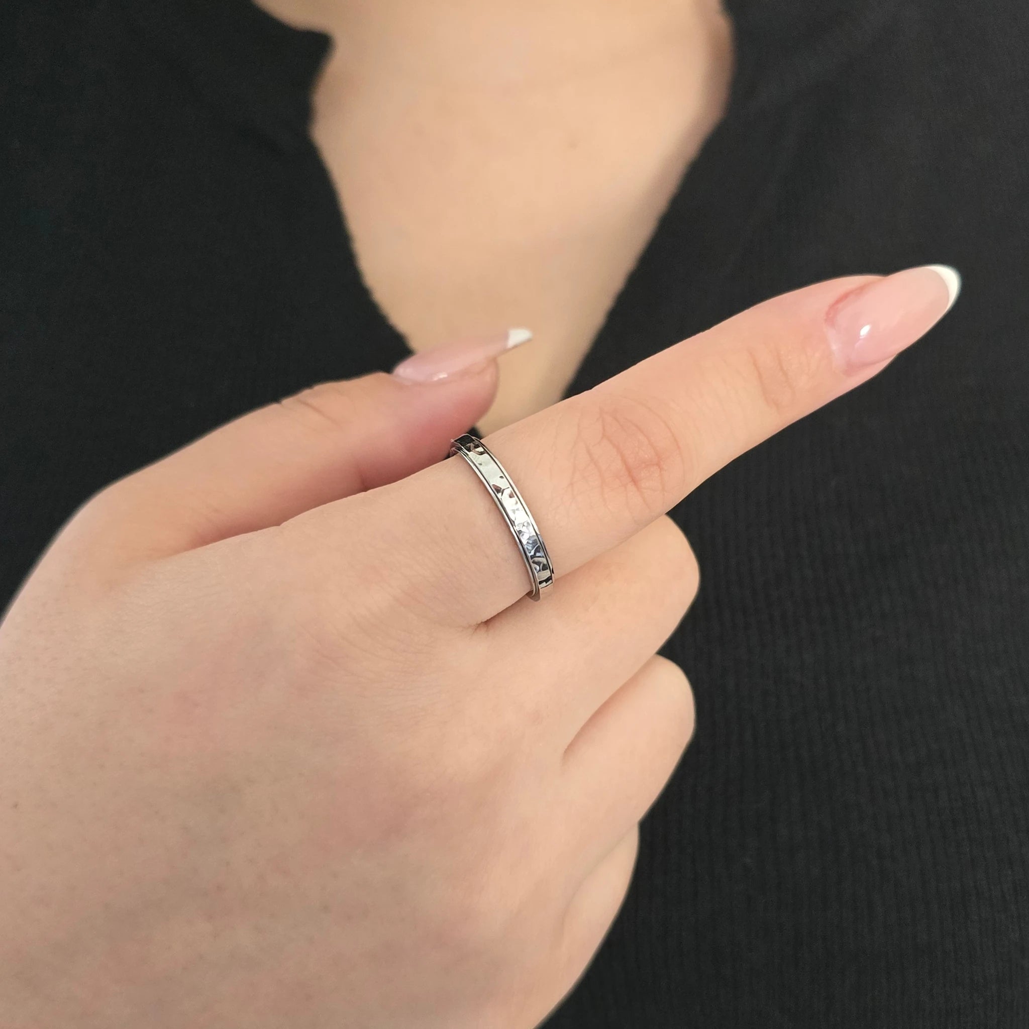 Elegante zilveren fidget ring met een lichtweerkaatsende gehamerde textuur, gedragen door een model met een chique zwart topje.