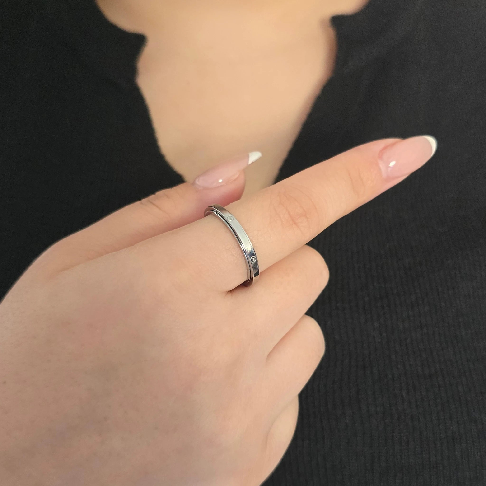 Elegante zilveren fidget ring met een strakke afwerking en een doorlopend golf-design, gedragen door een model met een chique zwart topje.