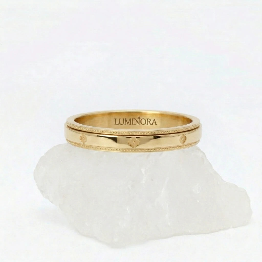 Gouden Fortuna fidget ring van RVS met een draaibaar klaver patroon, elegant rustend op een witte steen