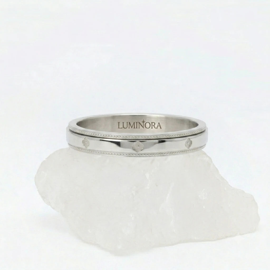 Zilveren Fortuna fidget ring van RVS met een roterende band voorzien van gegraveerd klaver patroon, gepresenteerd op een witte steen