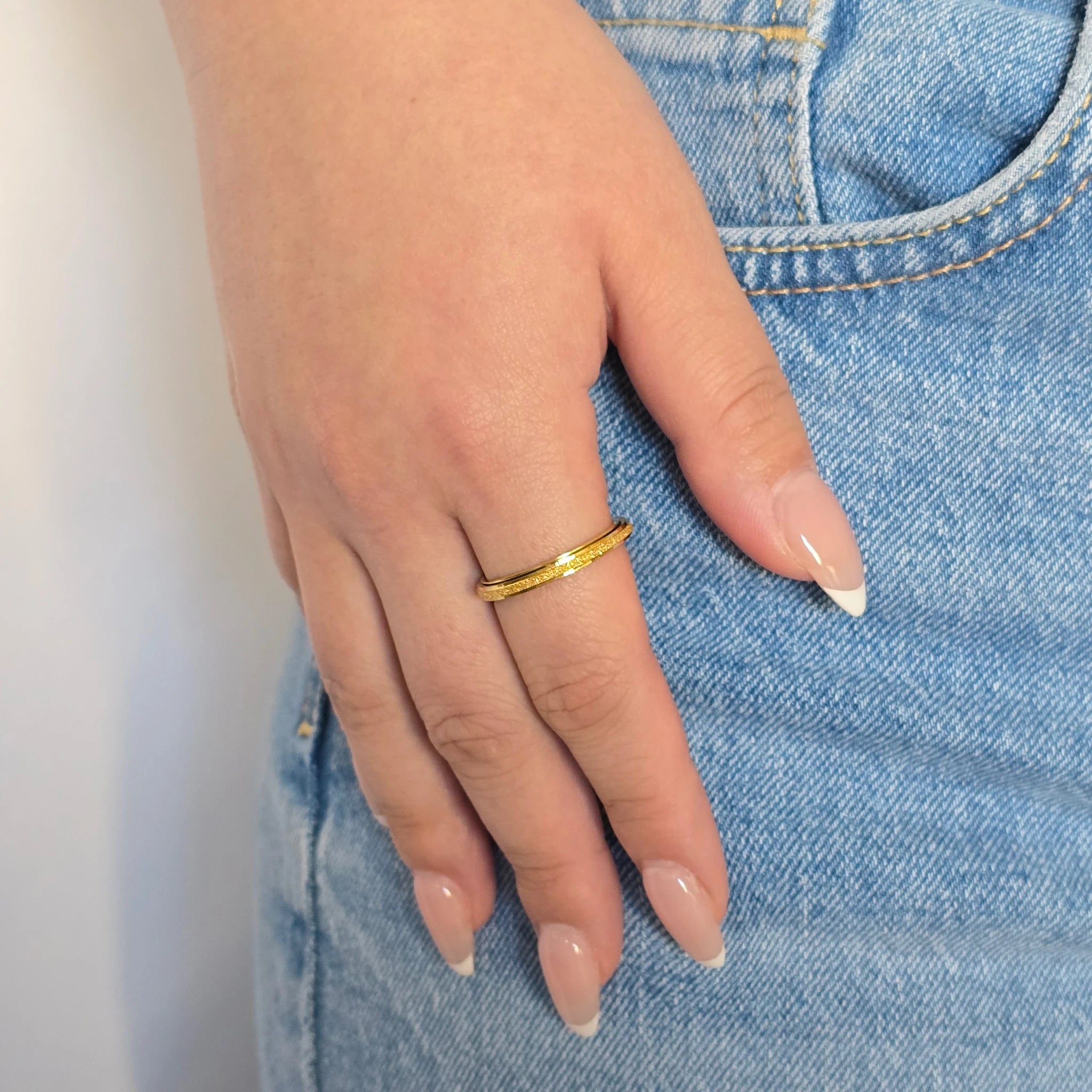 Hand van een vrouw in een blauwe jeans met een draagbare gouden anti-stress ring aan haar vinger.