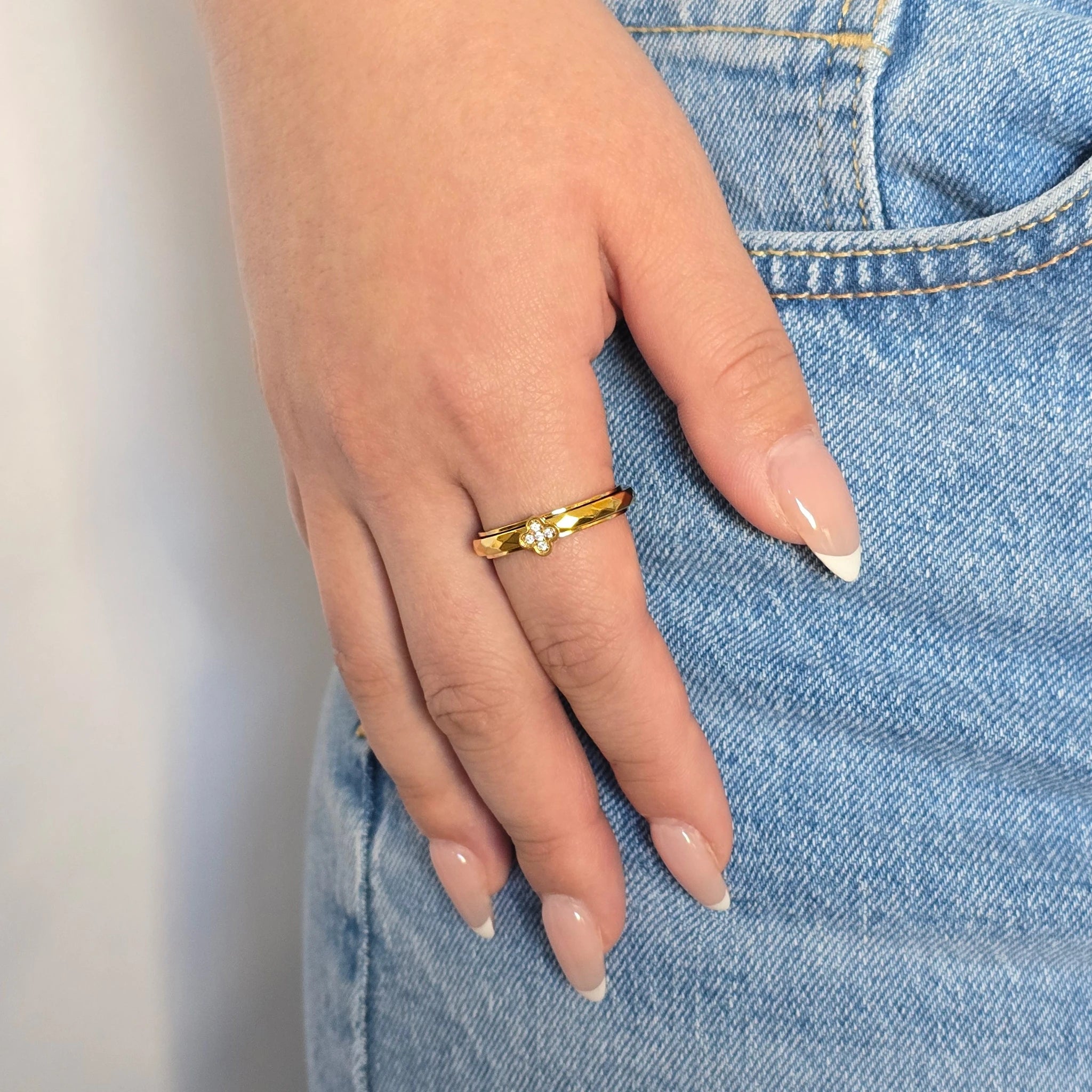 Hand van een vrouw in een casual blauwe spijkerbroek met een elegante gouden Clover anti-stress ring met een klavertje vier om haar vinger.