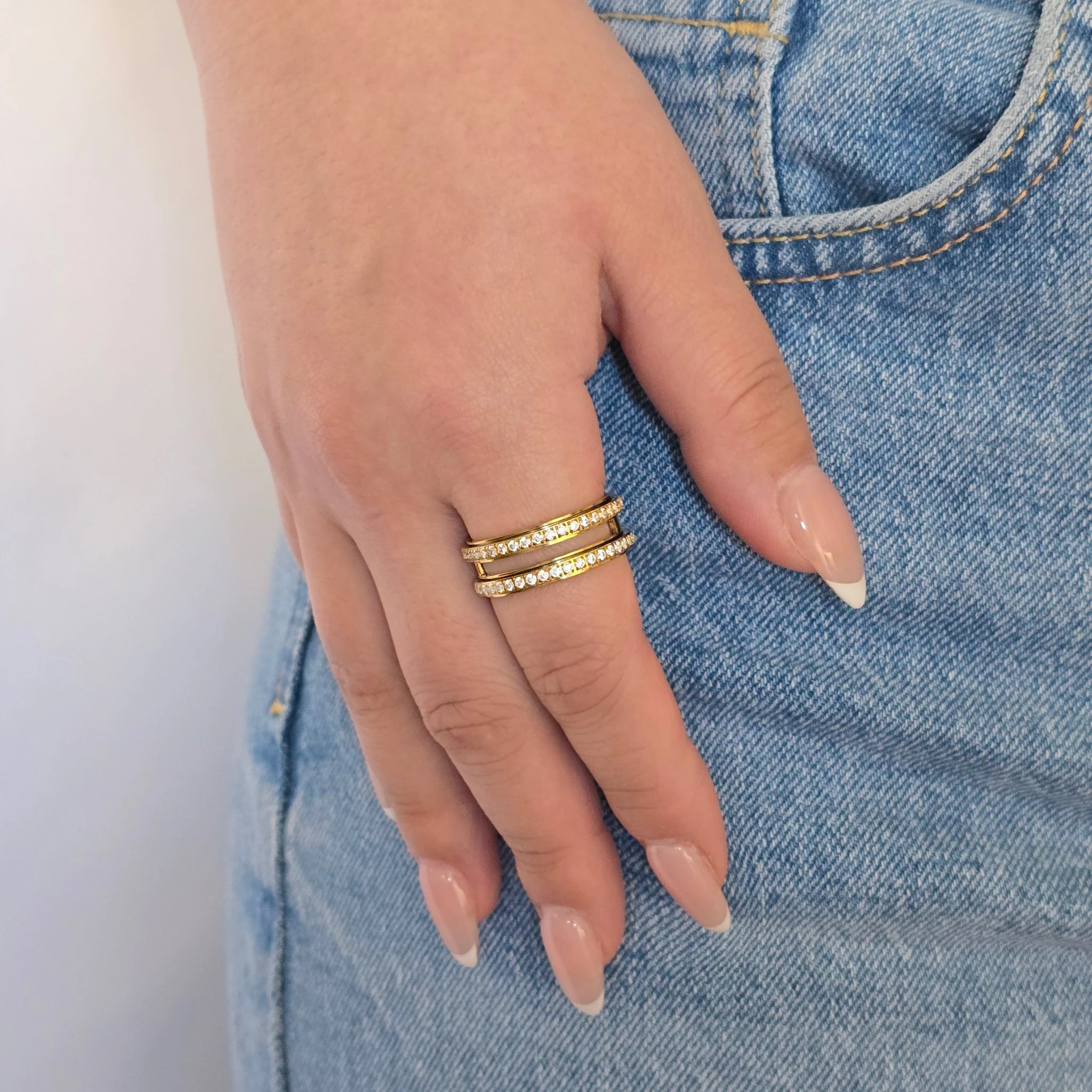 Hand van een vrouw in een casual blauwe jeans met een luxe gouden anti-stress ring met dubbele band aan haar vinger.