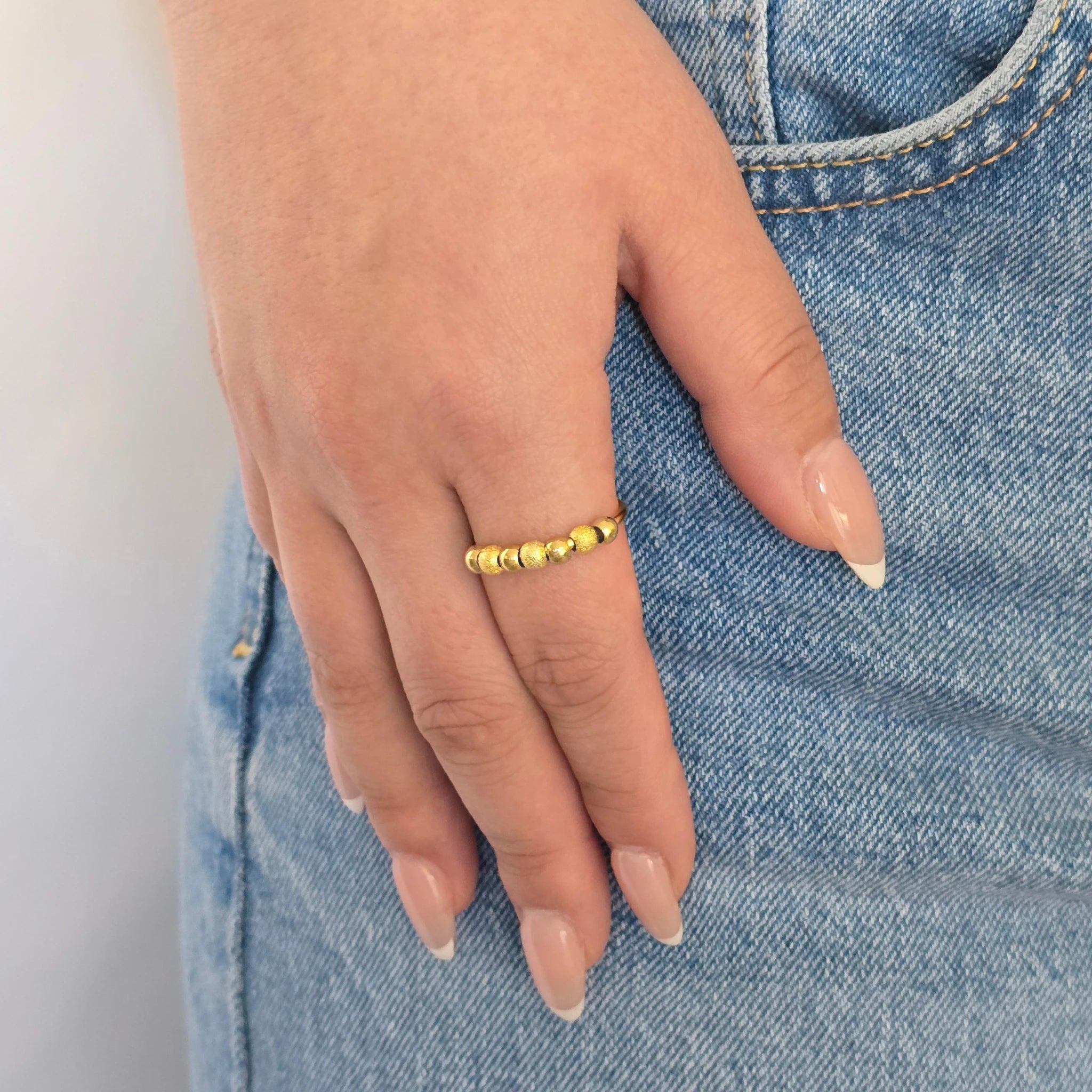 Hand van een vrouw in een casual blauwe jeans met een stijlvolle gouden anti-stress ring met balletjes aan haar vinger.