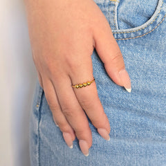 Hand van een vrouw in een blauwe jeans met een gouden anti-stress ring met kralen aan haar vinger.