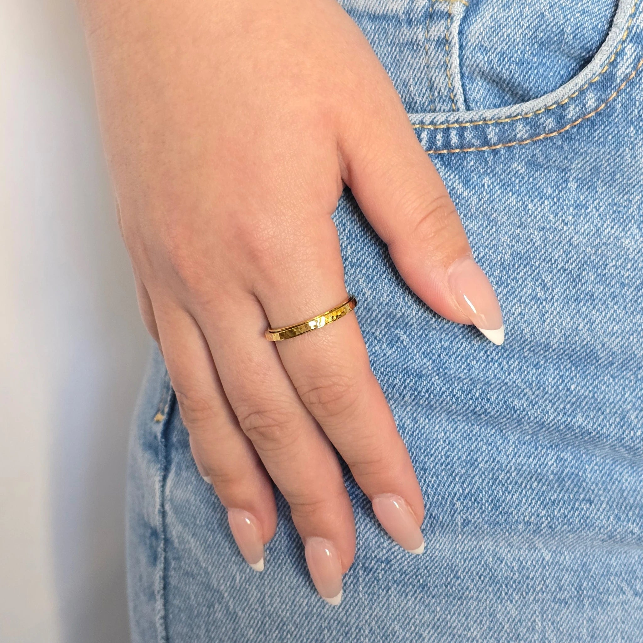 Hand van een vrouw in een casual blauwe jeans met een stijlvolle gouden anti-stress ring met gehamerde details aan haar vinger.