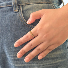 Hand van een vrouw met de gouden Classic Bead anti-stress ring met roterende kralen, gefotografeerd op een blauwe jeans.