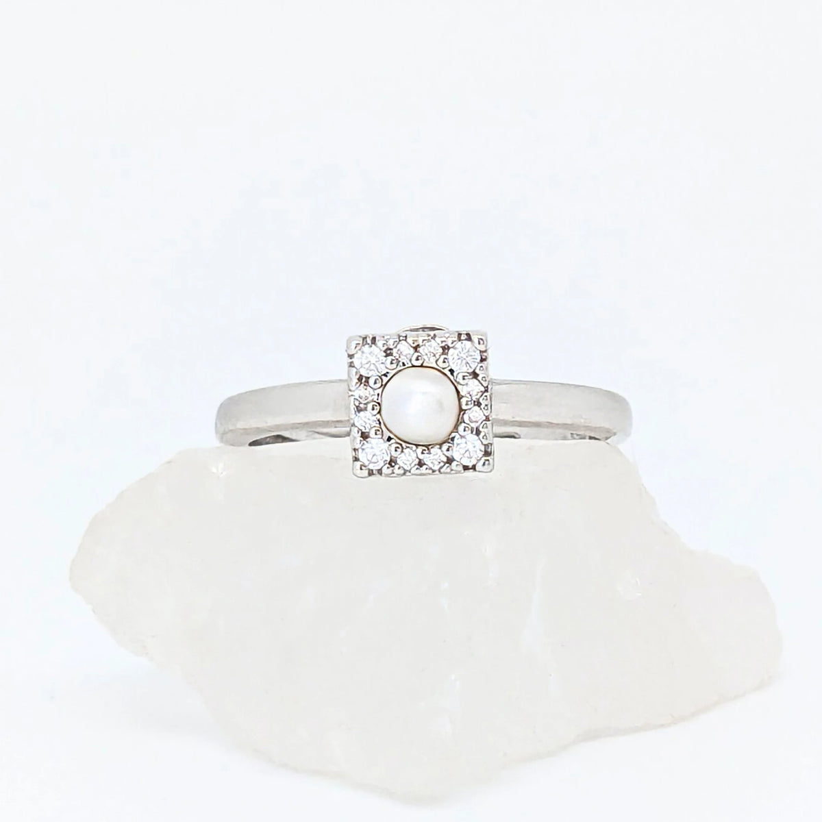 Zilveren Halo fidget ring met een glanzende parel in een vierkant frame, gepresenteerd op een witte ruwe steen.