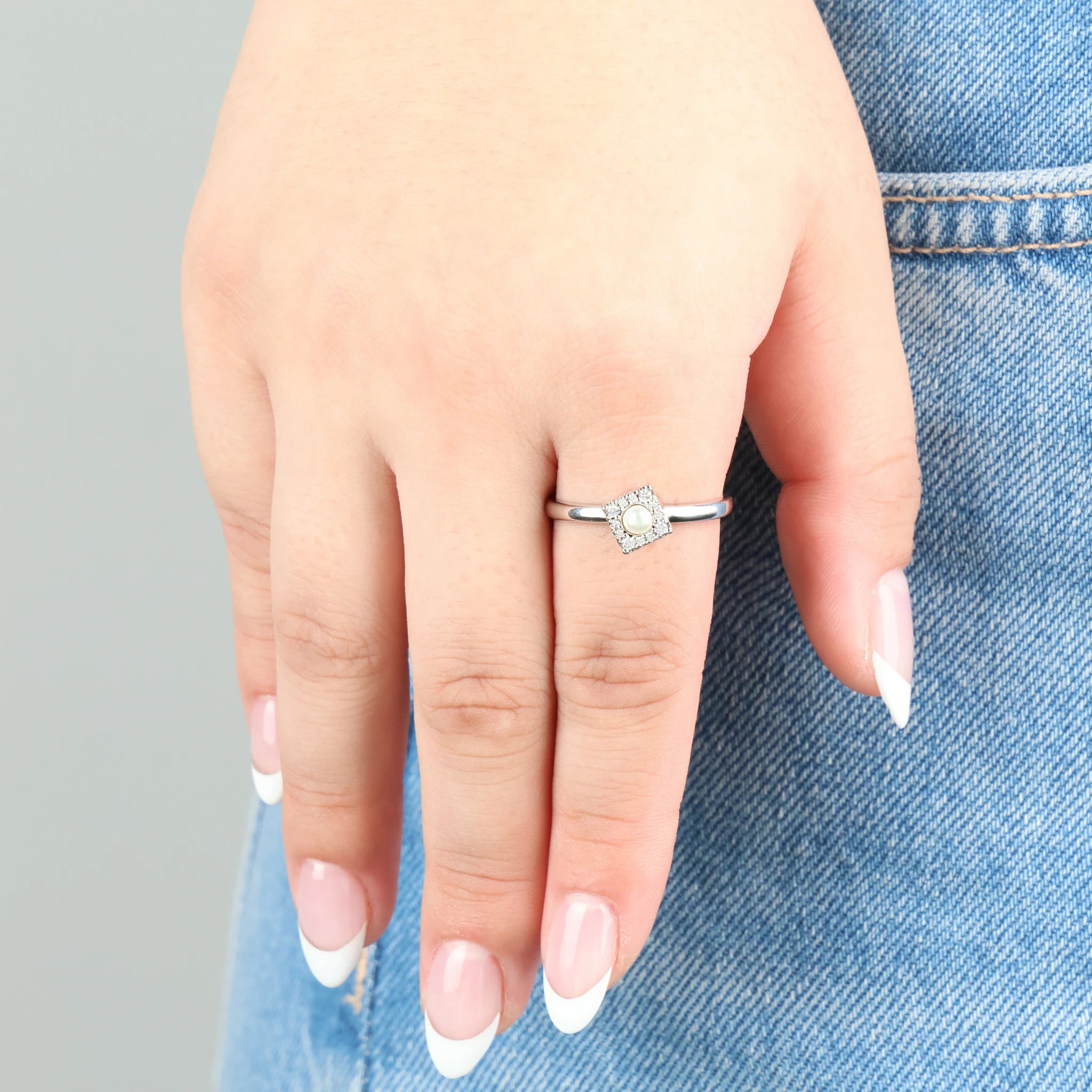 Close-up van de zilveren Halo stress ring met vierkant design en zirkonia steentjes gedragen op een jeans.