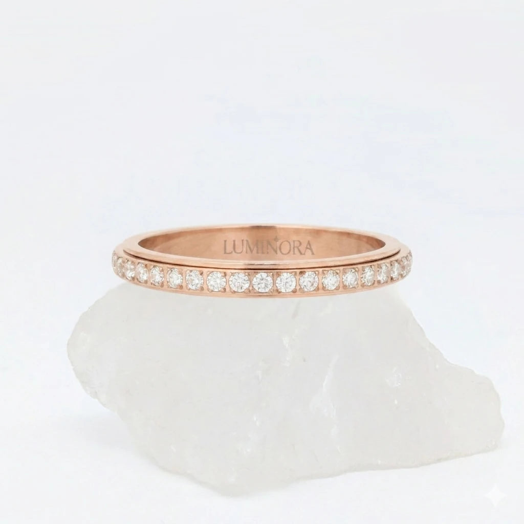 Roségouden Haven fidget ring van waterproof roestvrij staal, afgewerkt met een roterende band vol schitterende steentjes, gepresenteerd op een witte steen.