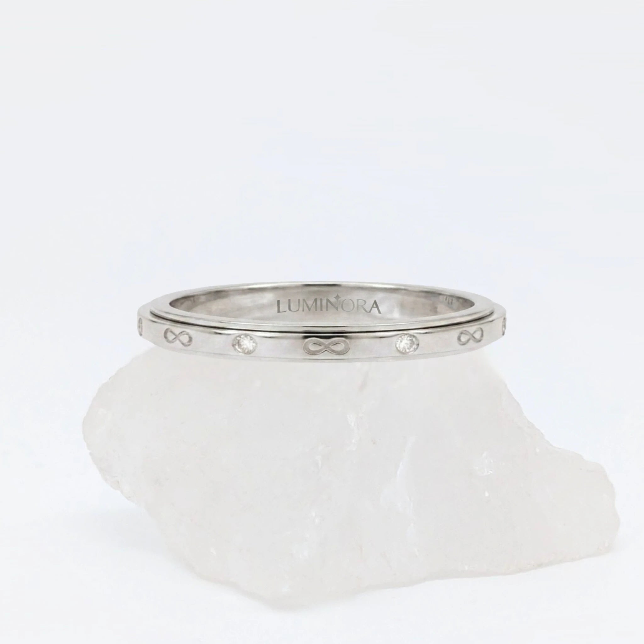 Zilveren Infinity anxiety ring ontworpen met elegante oneindigheidssymbolen en steentjes, geplaatst op een witte kwartssteen.