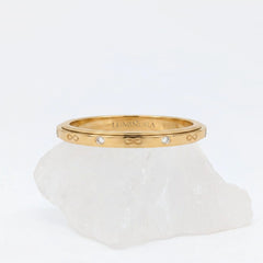 Gouden Infinity fidget ring met gegraveerde oneindigheidssymbolen en subtiele kristallen, gepresenteerd op een witte steen.