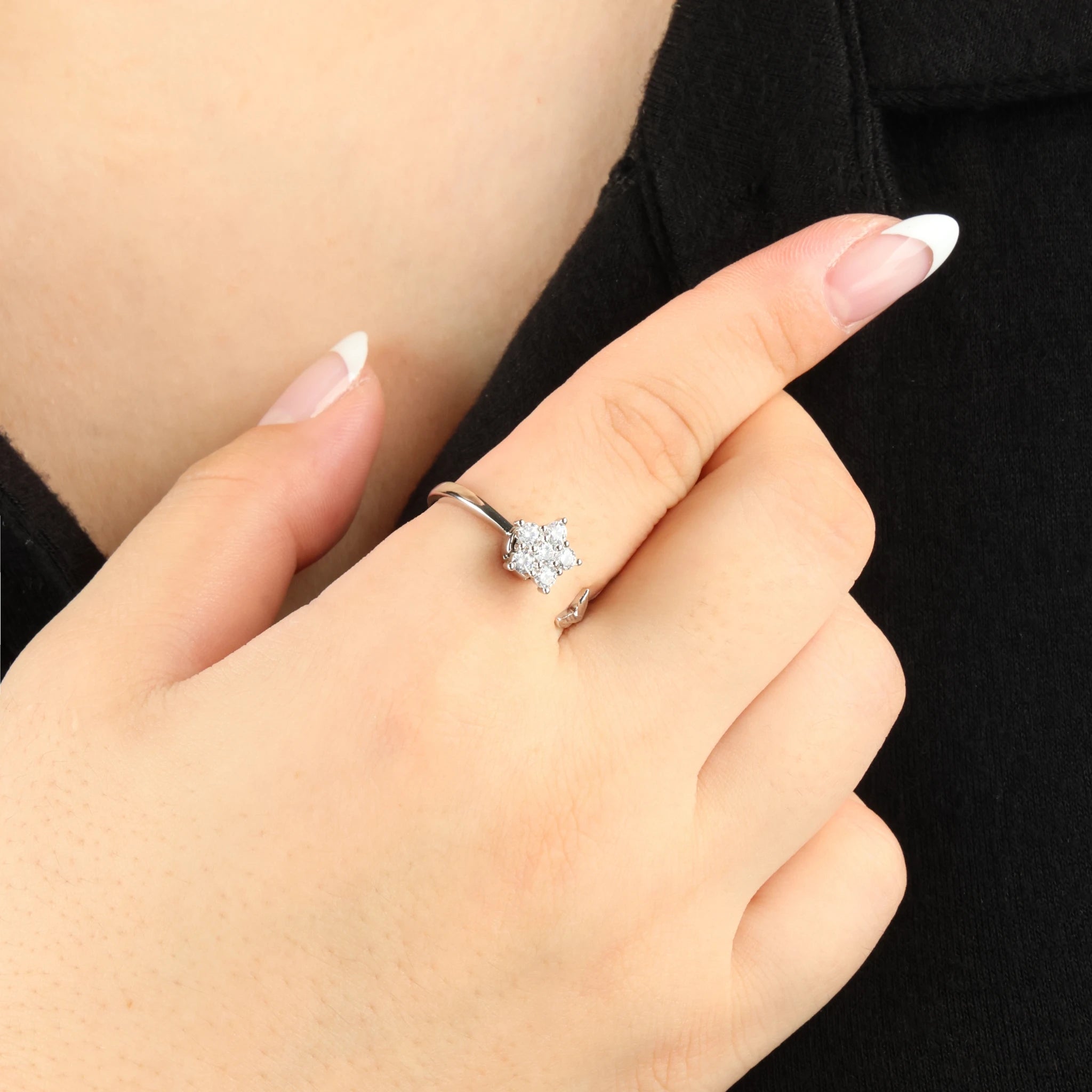 Zilveren Iris anxiety ring met een draaiend bloemetje om de vinger gefotografeerd tegen een contrasterend zwart shirt.