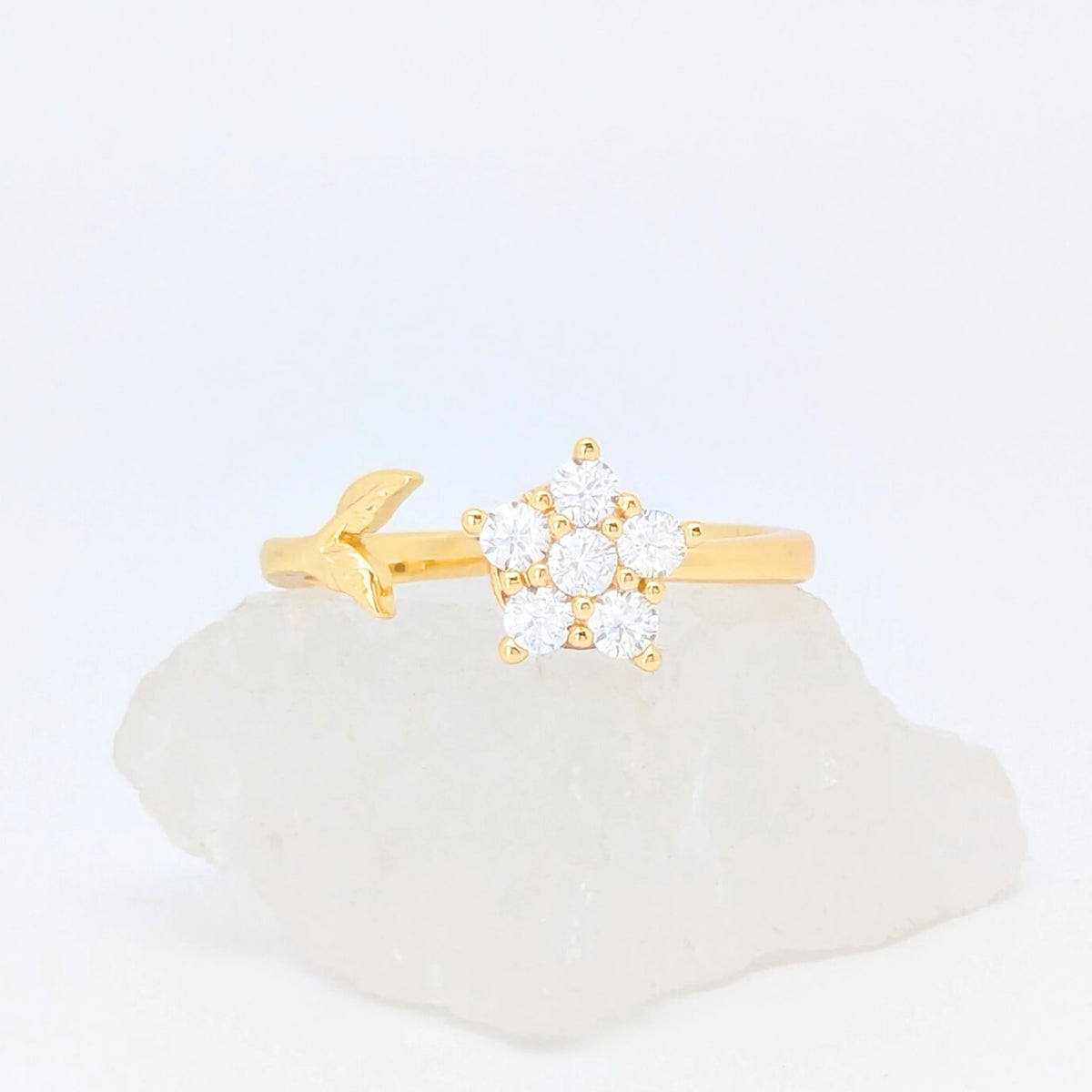 Gouden Iris fidget ring in de vorm van een bloem en een subtiel takje gepresenteerd op een witte ruwe steen.