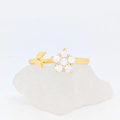 Gouden Iris fidget ring in de vorm van een bloem en een subtiel takje gepresenteerd op een witte ruwe steen.