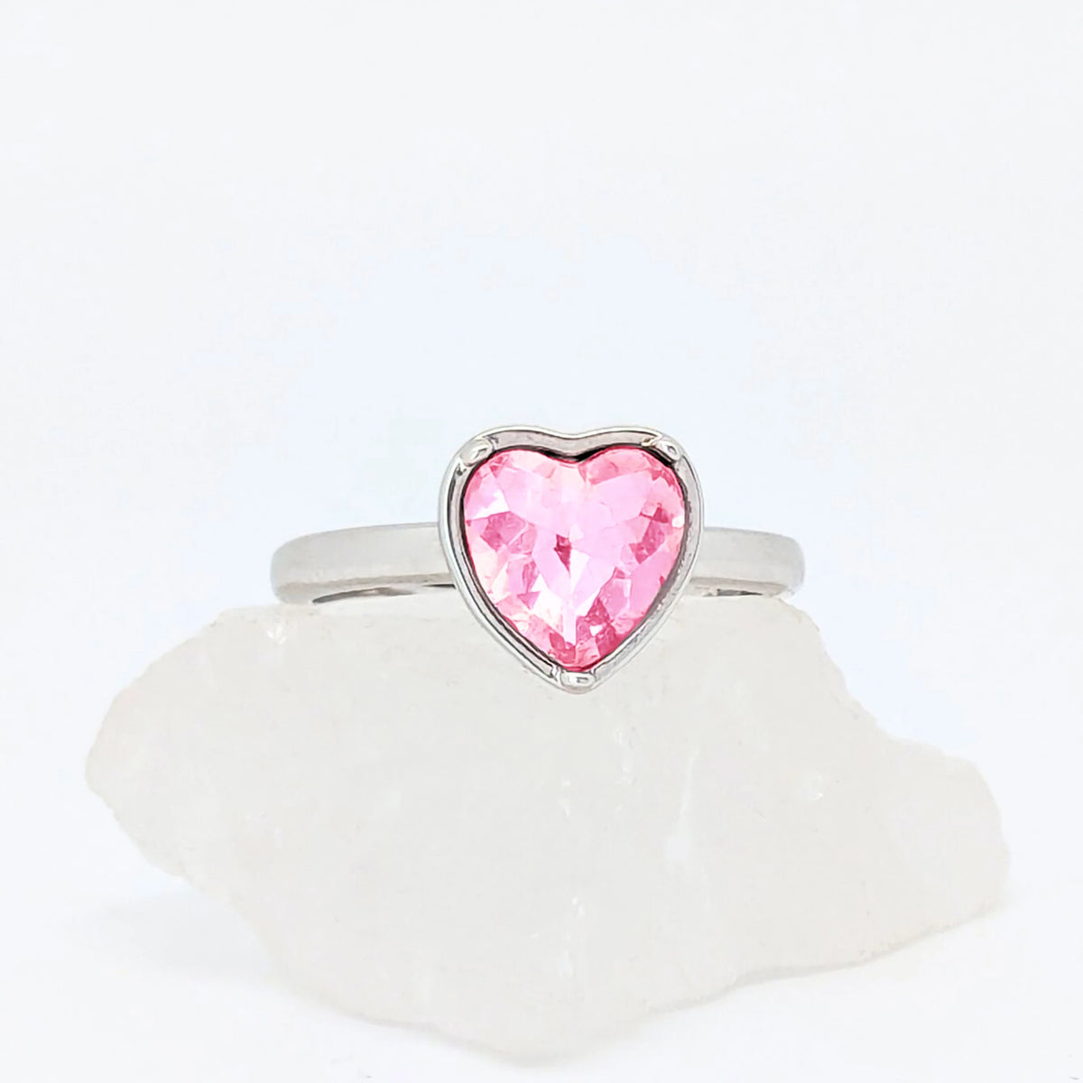 Zilveren Love fidget ring met een groot roze kristal in de vorm van een hart, liggend op een witte steen.