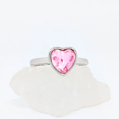 Zilveren Love fidget ring met een groot roze kristal in de vorm van een hart, liggend op een witte steen.
